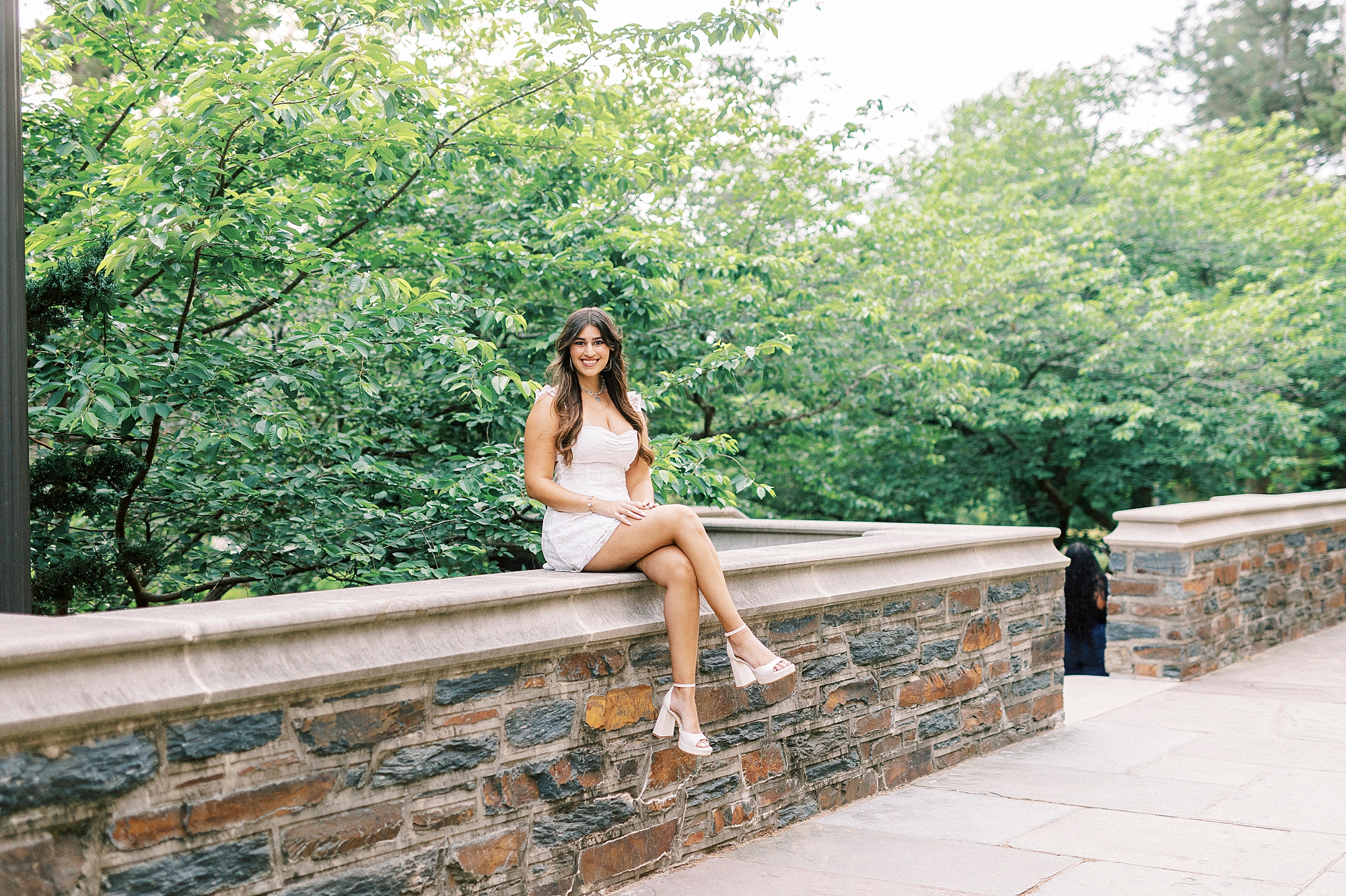 brunette college senior sits on brick wall during Duke Chapel graduation portraits