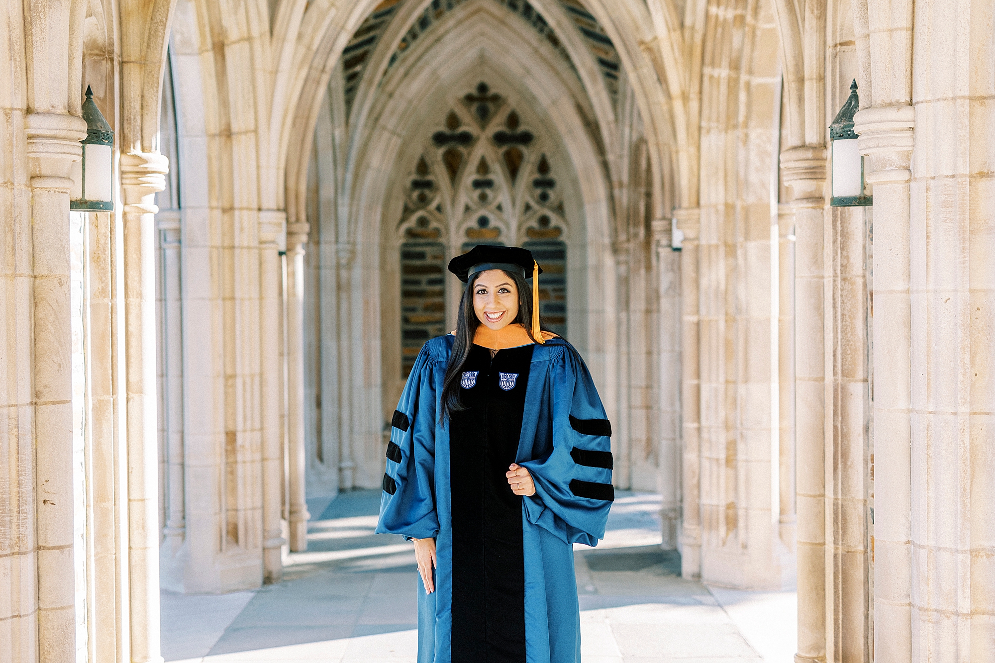 woman stands in blue and black cap and gown during graduation portraits at Duke University