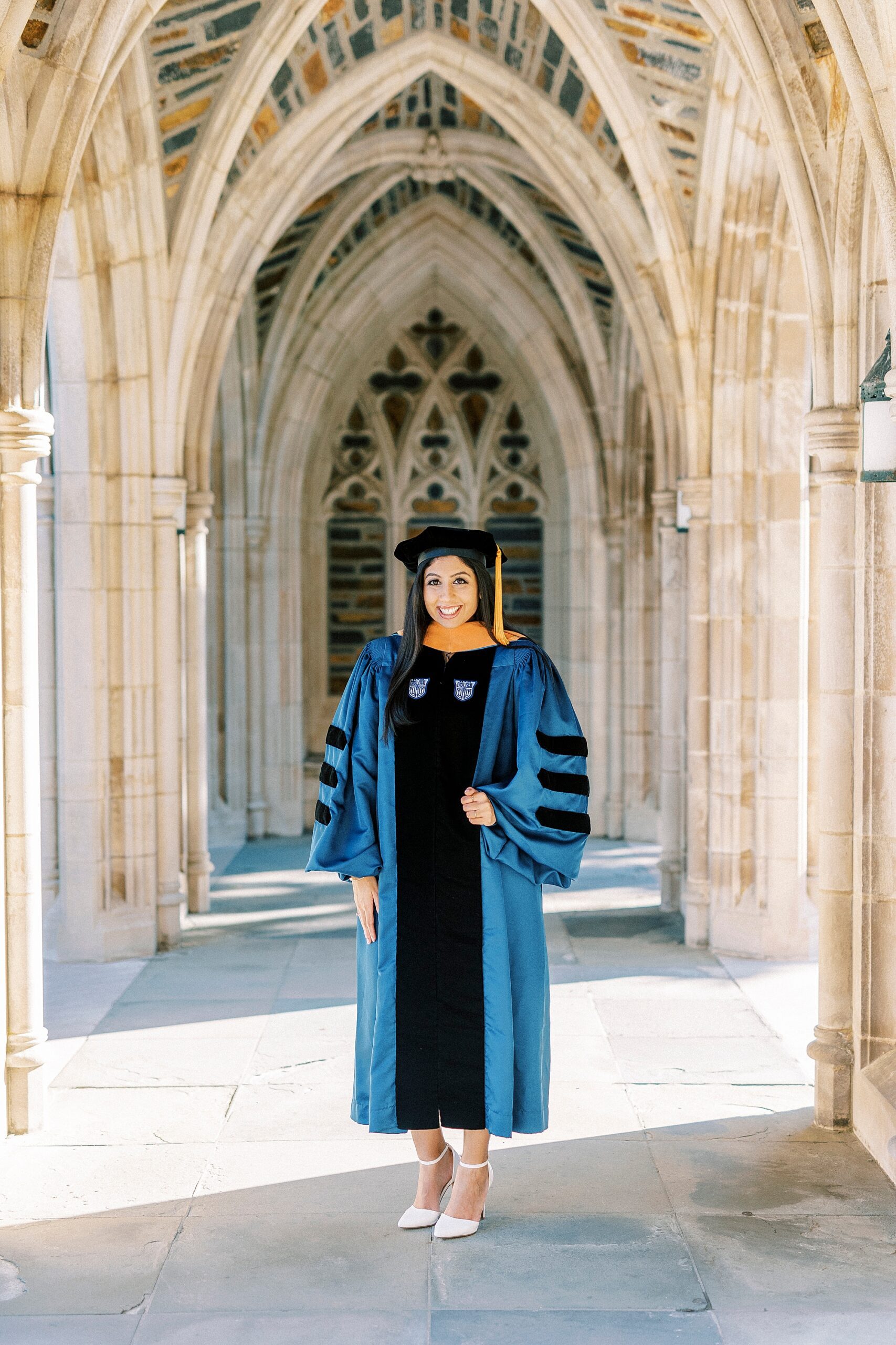 woman poses with hands on hip in blue and black gown during graduation portraits at Duke University
