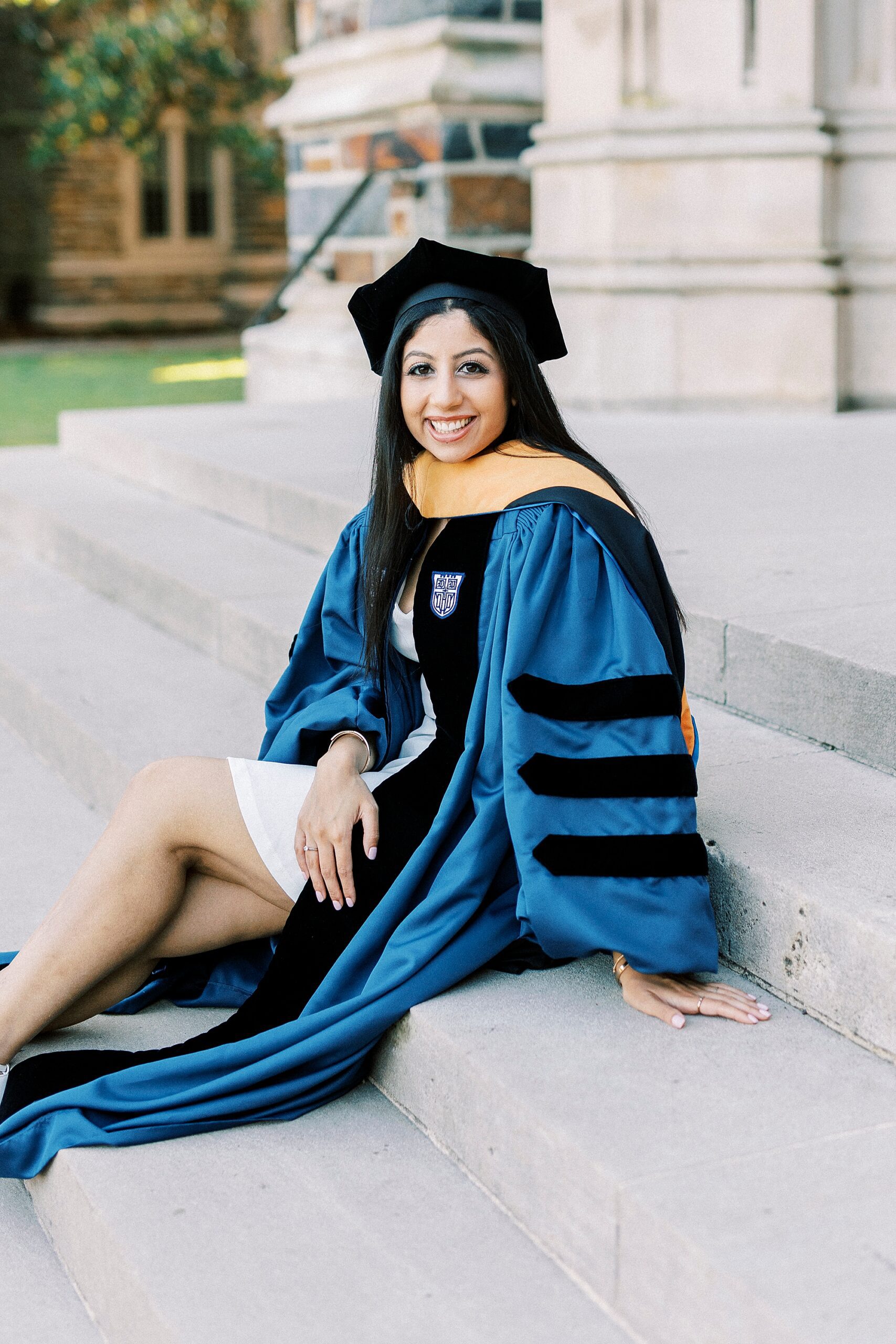 woman sits on steps showing off white dress under cap and gown