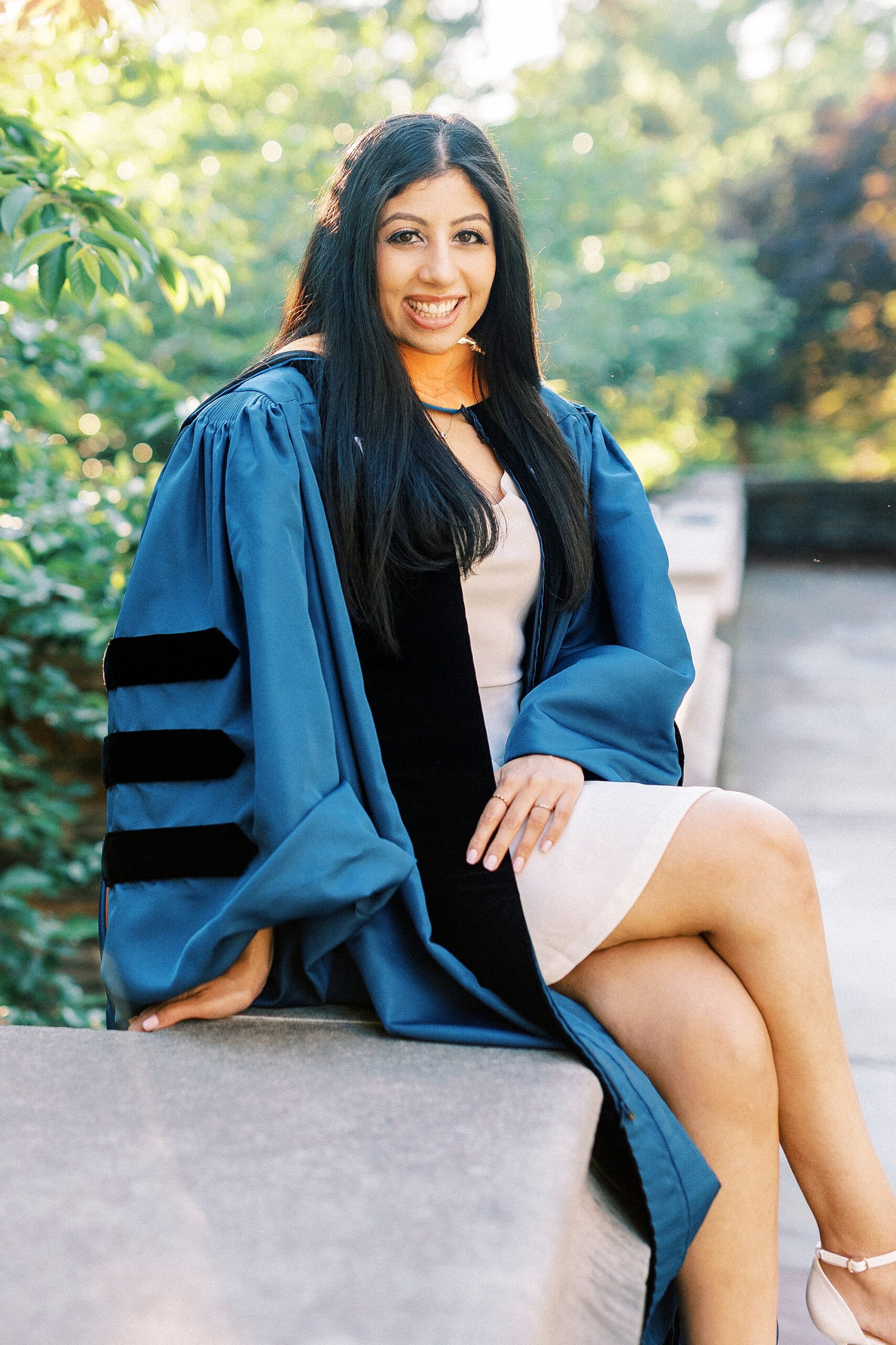 graduate sits on stone wall during graduation portraits at Duke University