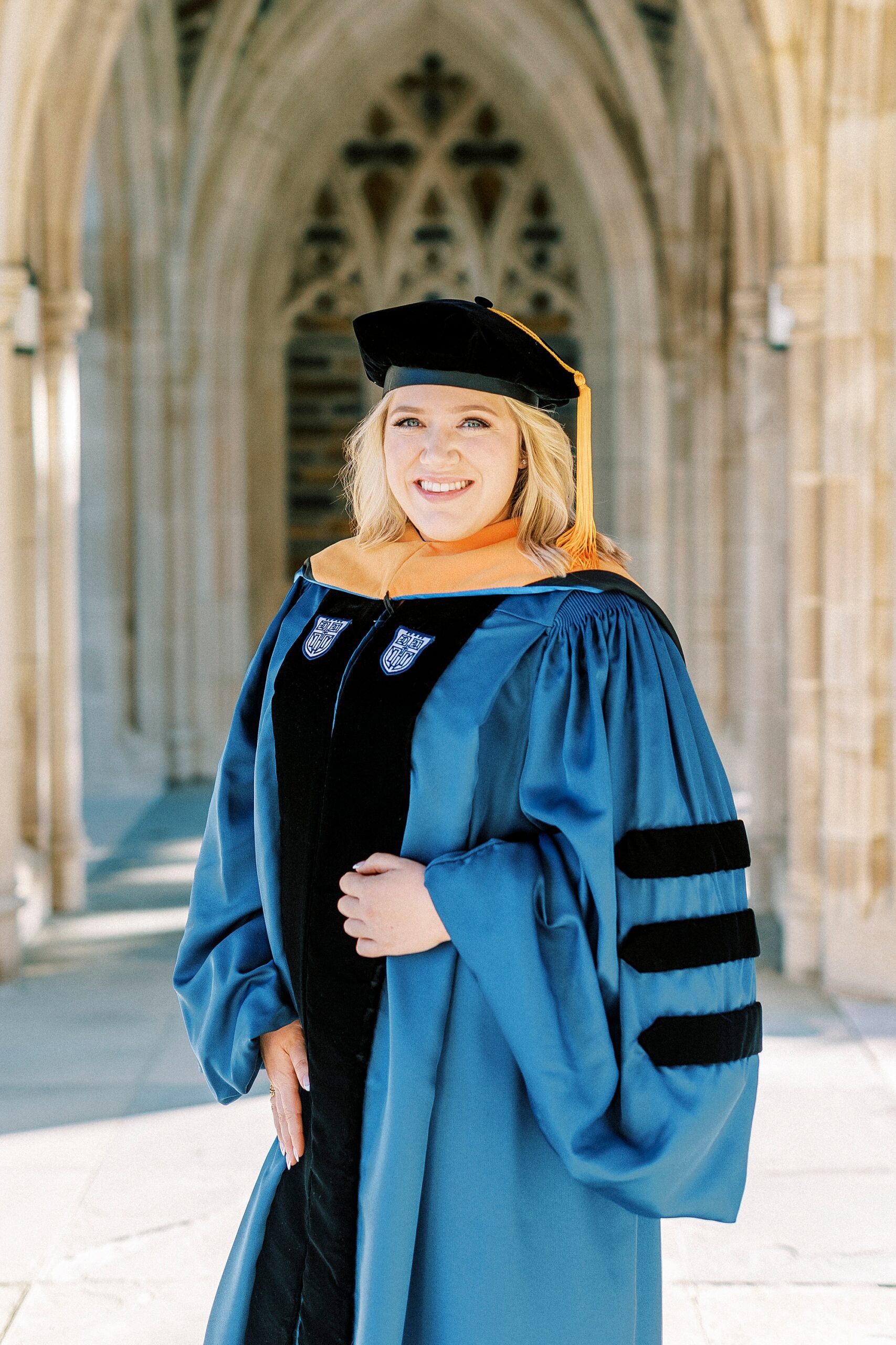 woman poses in blue and black cap and gown  during graduation portraits at Duke University