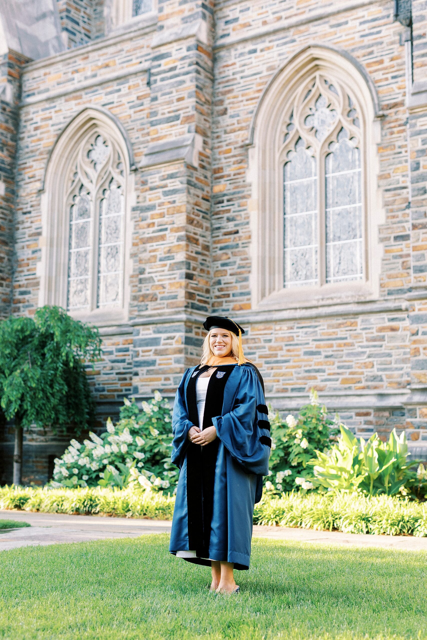 woman stands on grass outside Duke Chapel in hat and gown