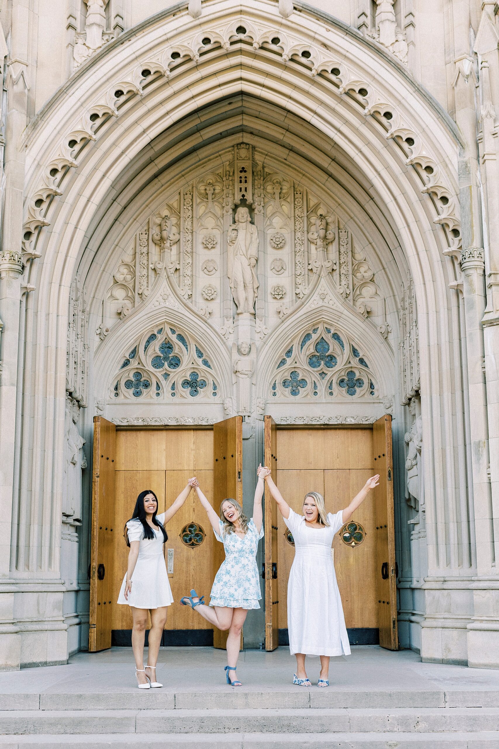 three friends hold hands cheering outside wooden doors at Duke Chapel 