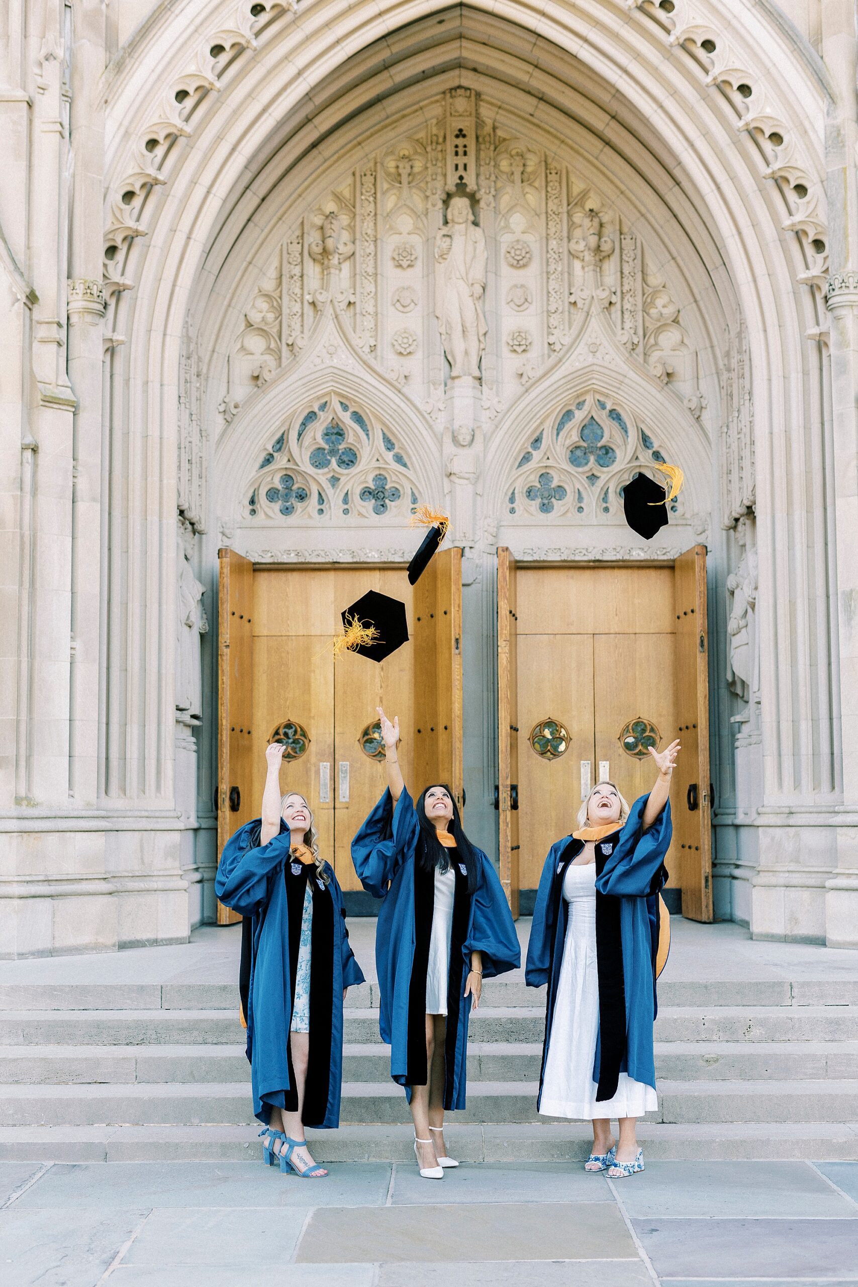three women toss cap and gown during graduation portraits at Duke University