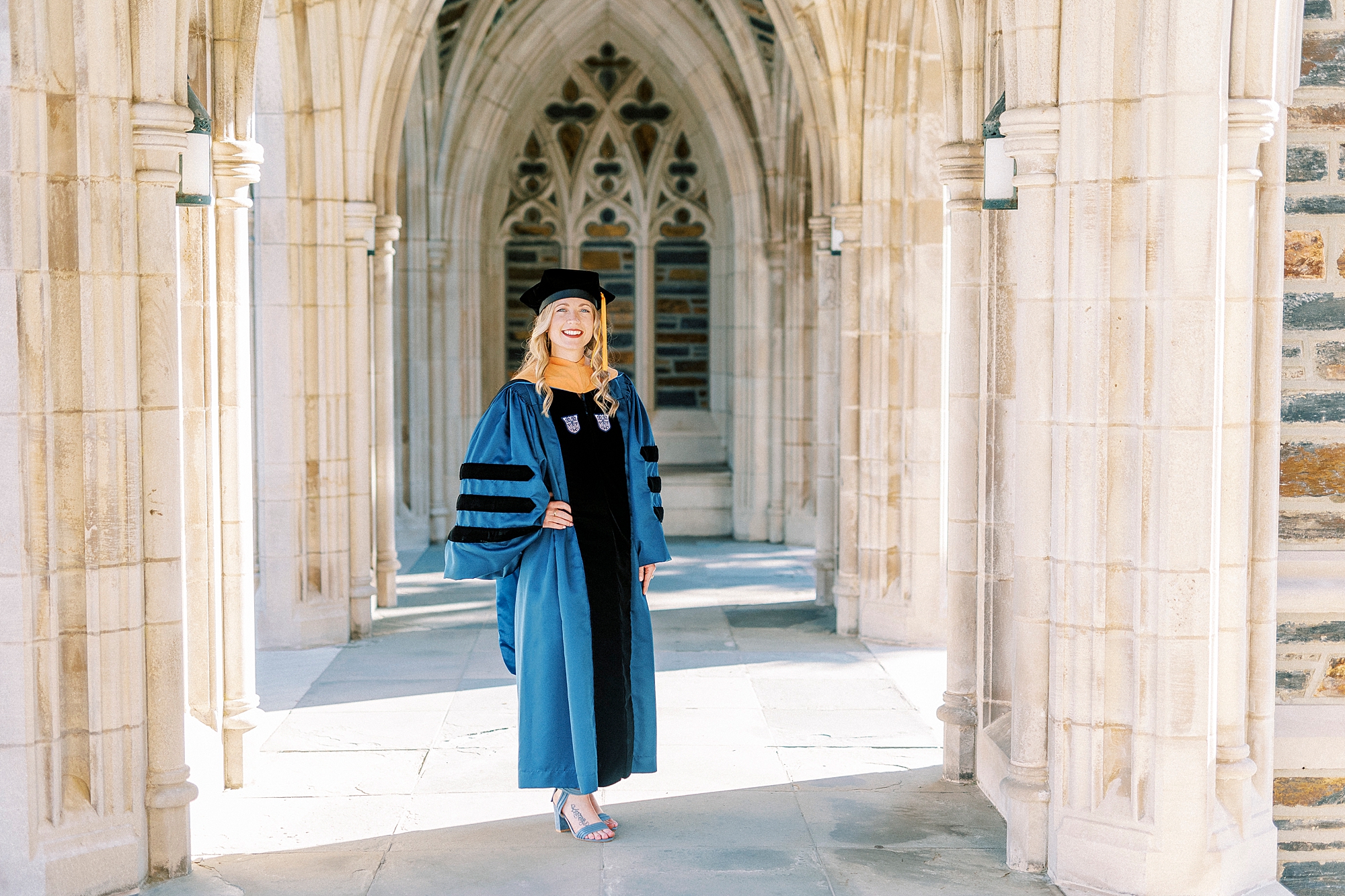 woman stands with hands on hips in black and blue gown during graduation portraits at Duke University
