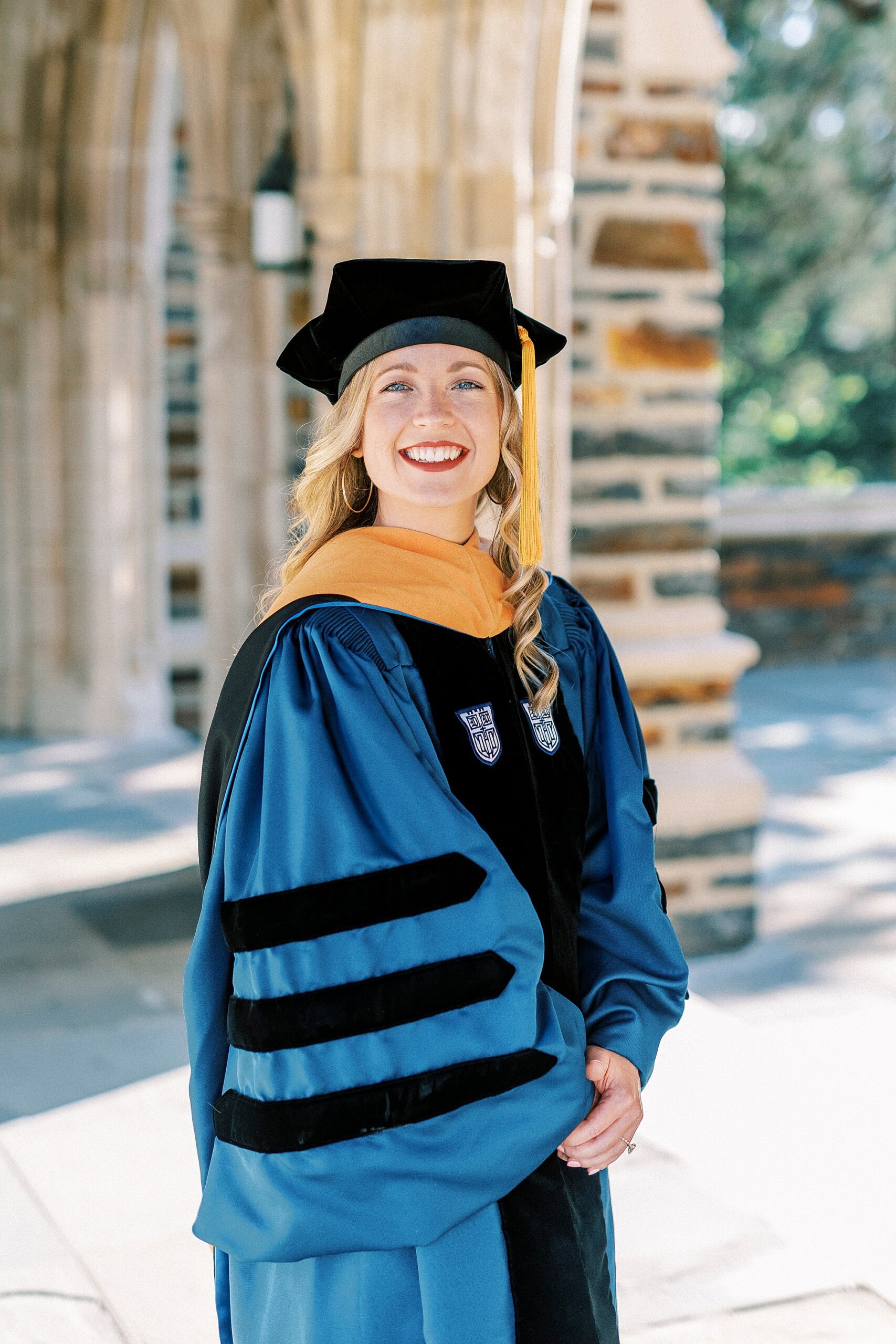  blonde woman smiles in graduation cap and gown during graduation portraits at Duke University