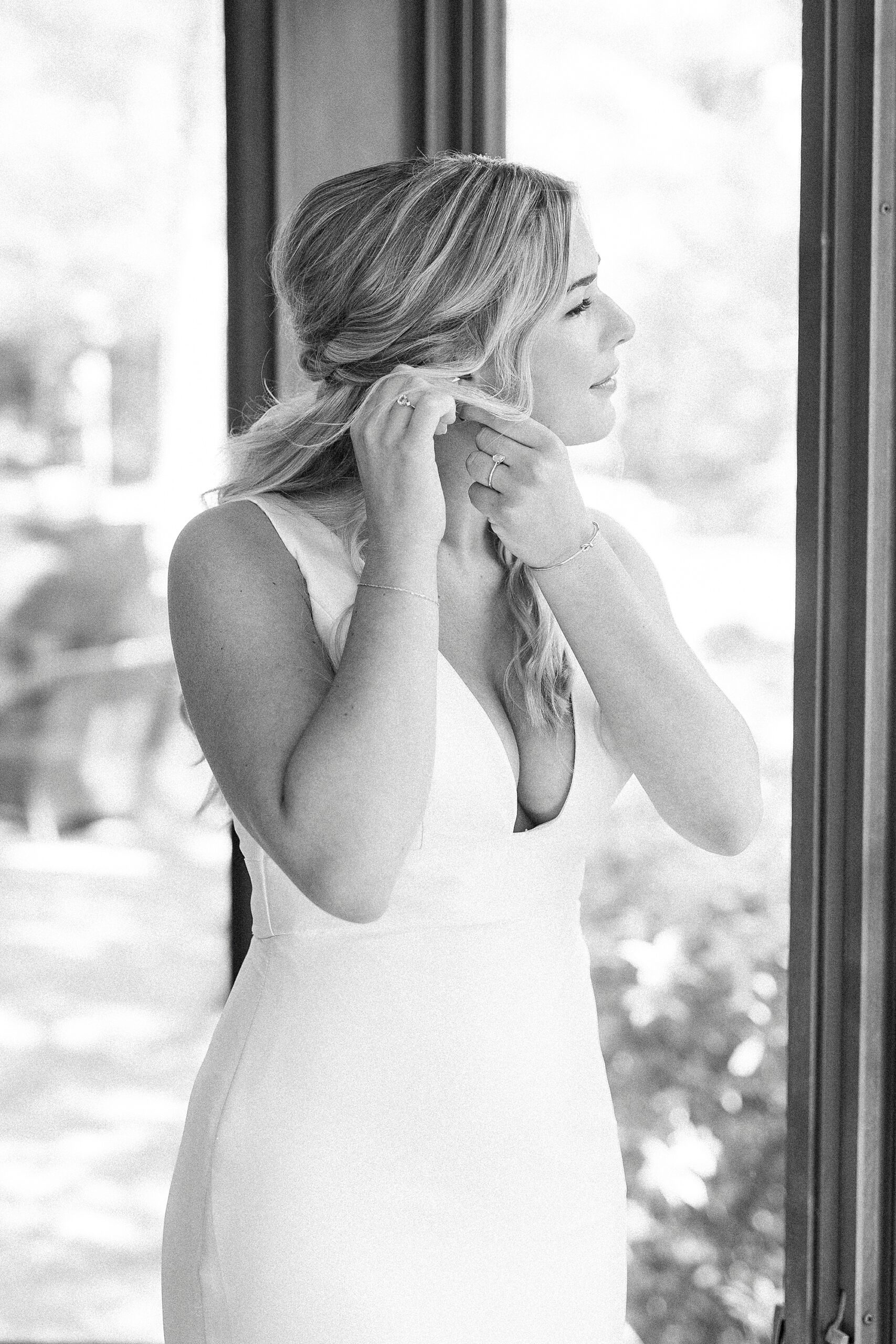 bride adjusts earrings while looking out window of Unionville NC home