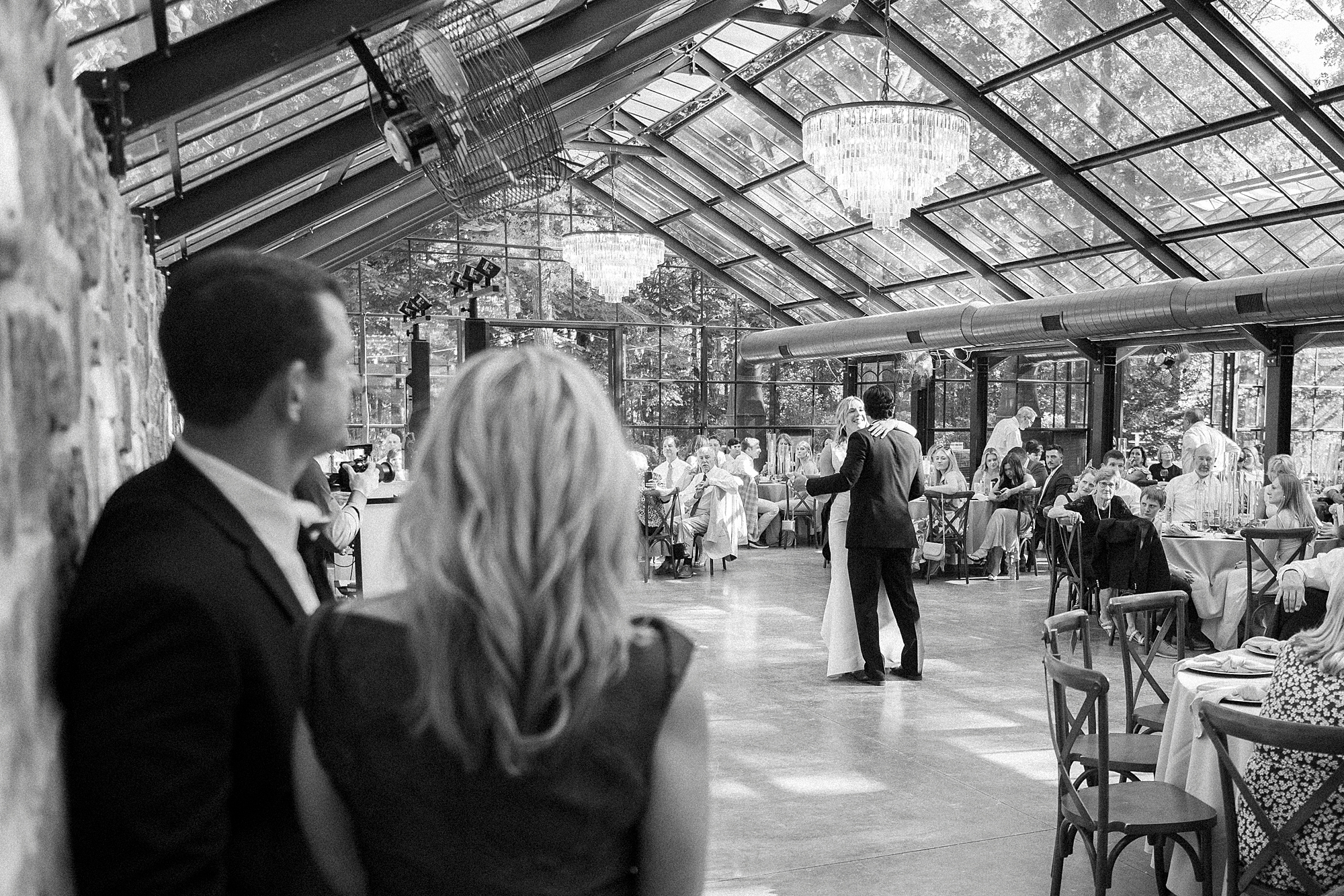 parents watch bride and groom dance in glass house at Morning Glory Farm