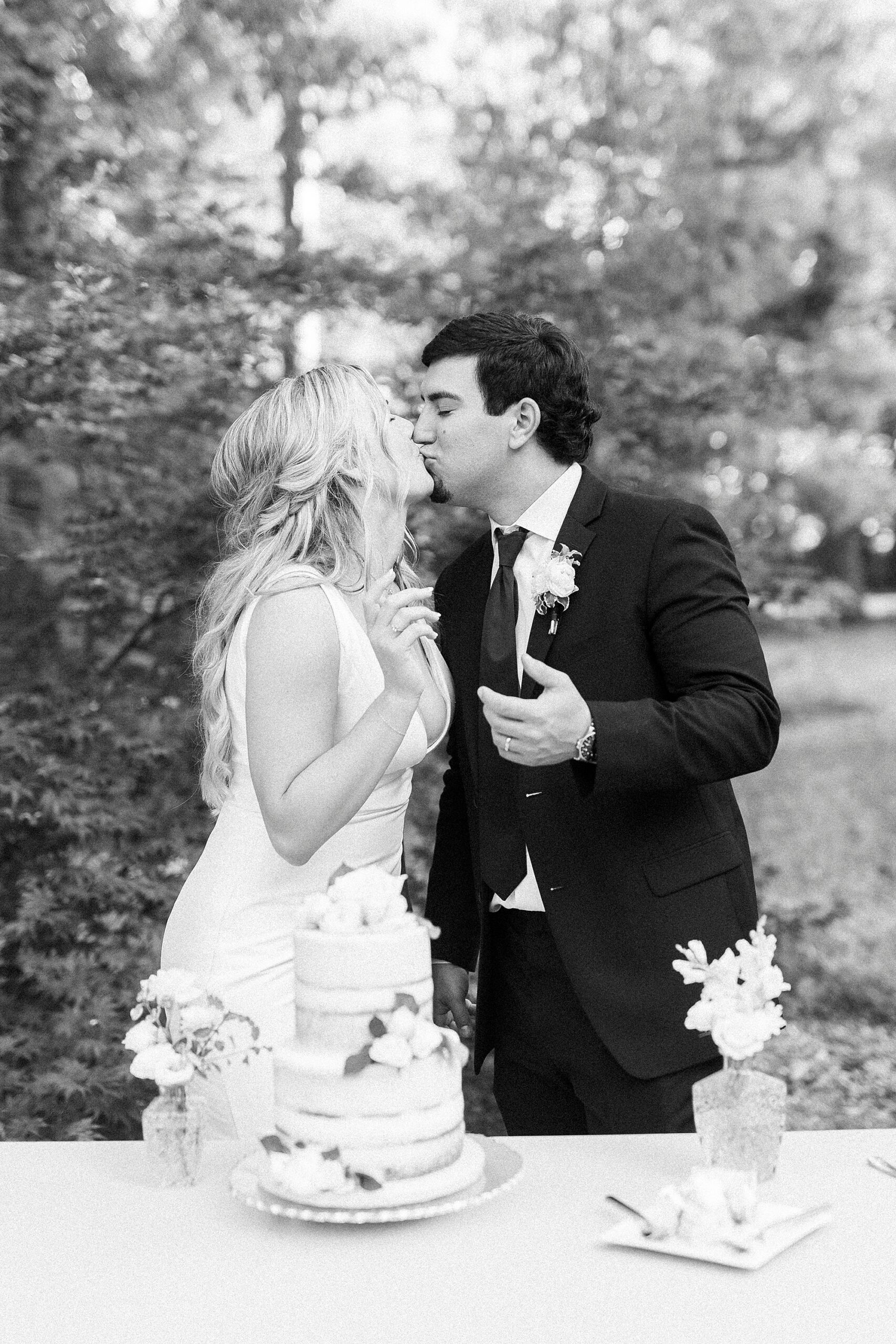 newlyweds kiss by wedding cake during NC wedding reception at Morning Glory Farm