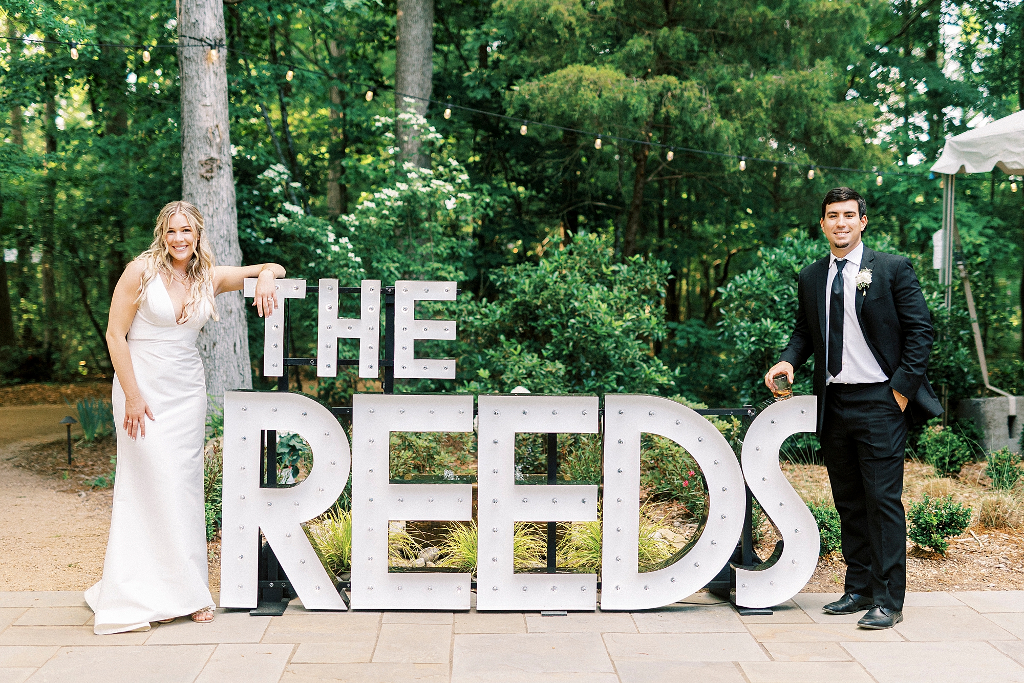 bride and groom stand next to white light letters saying THE REEDS