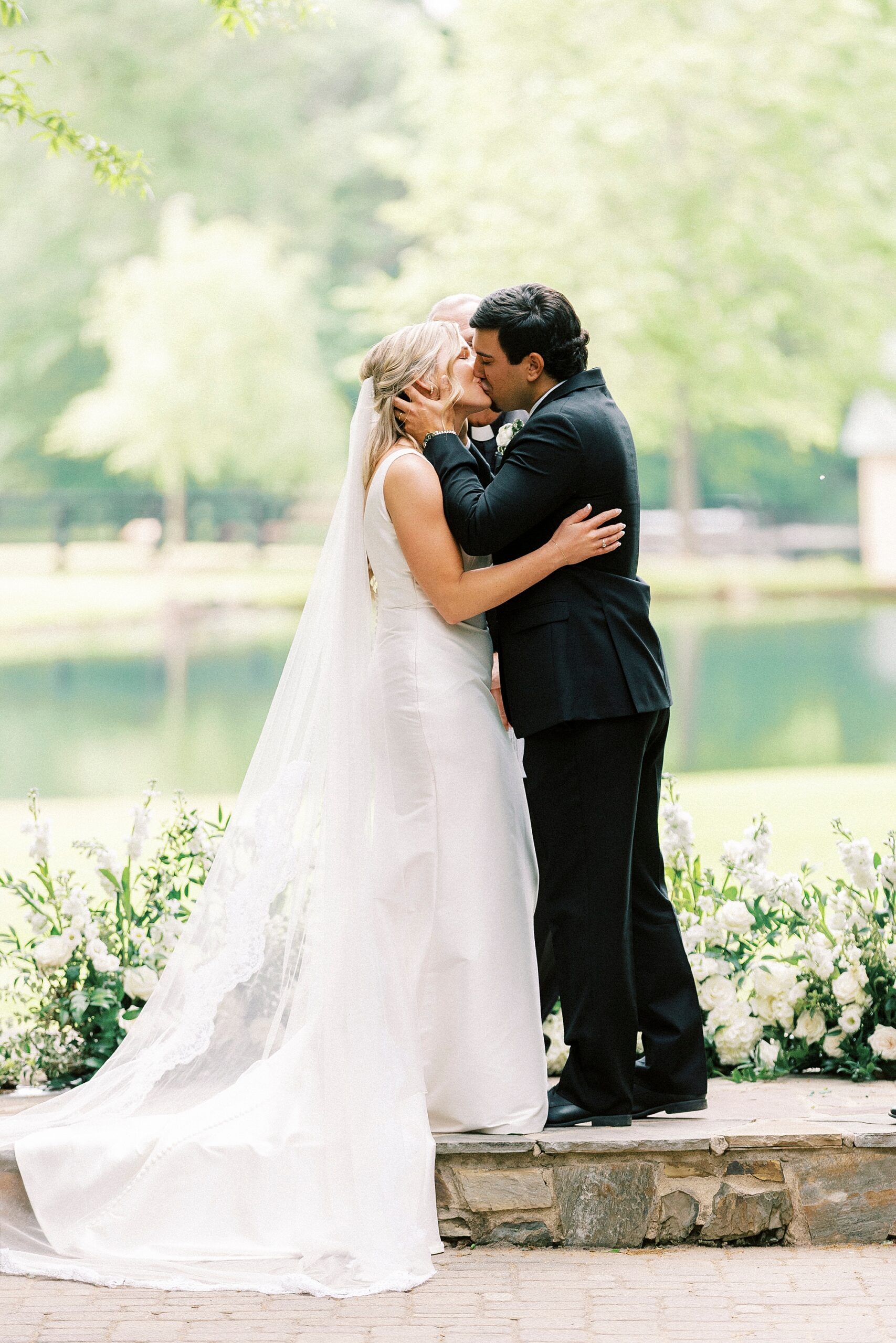 bride and groom kiss during ceremony by water at Morning Glory Farm