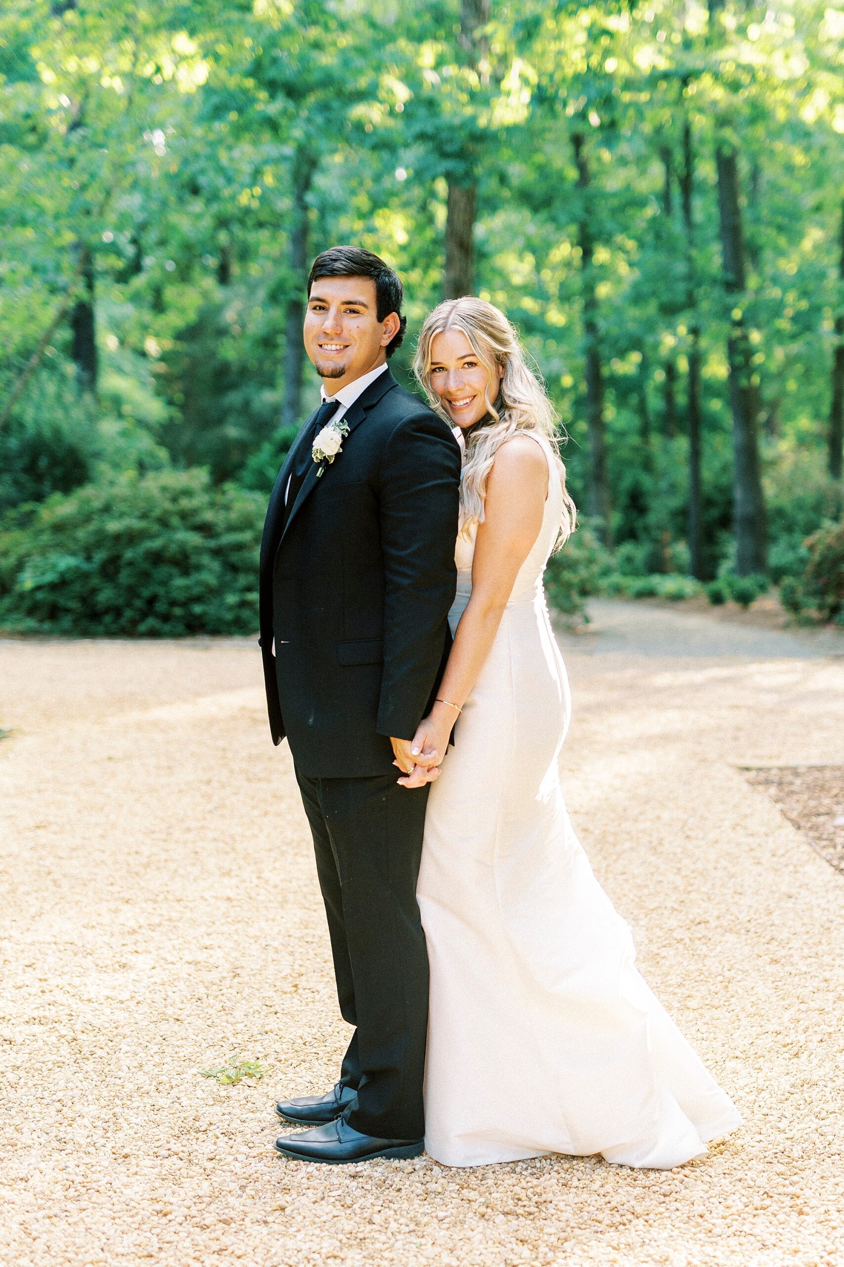 bride stands behind groom hugging him on dirt path at Morning Glory Farm