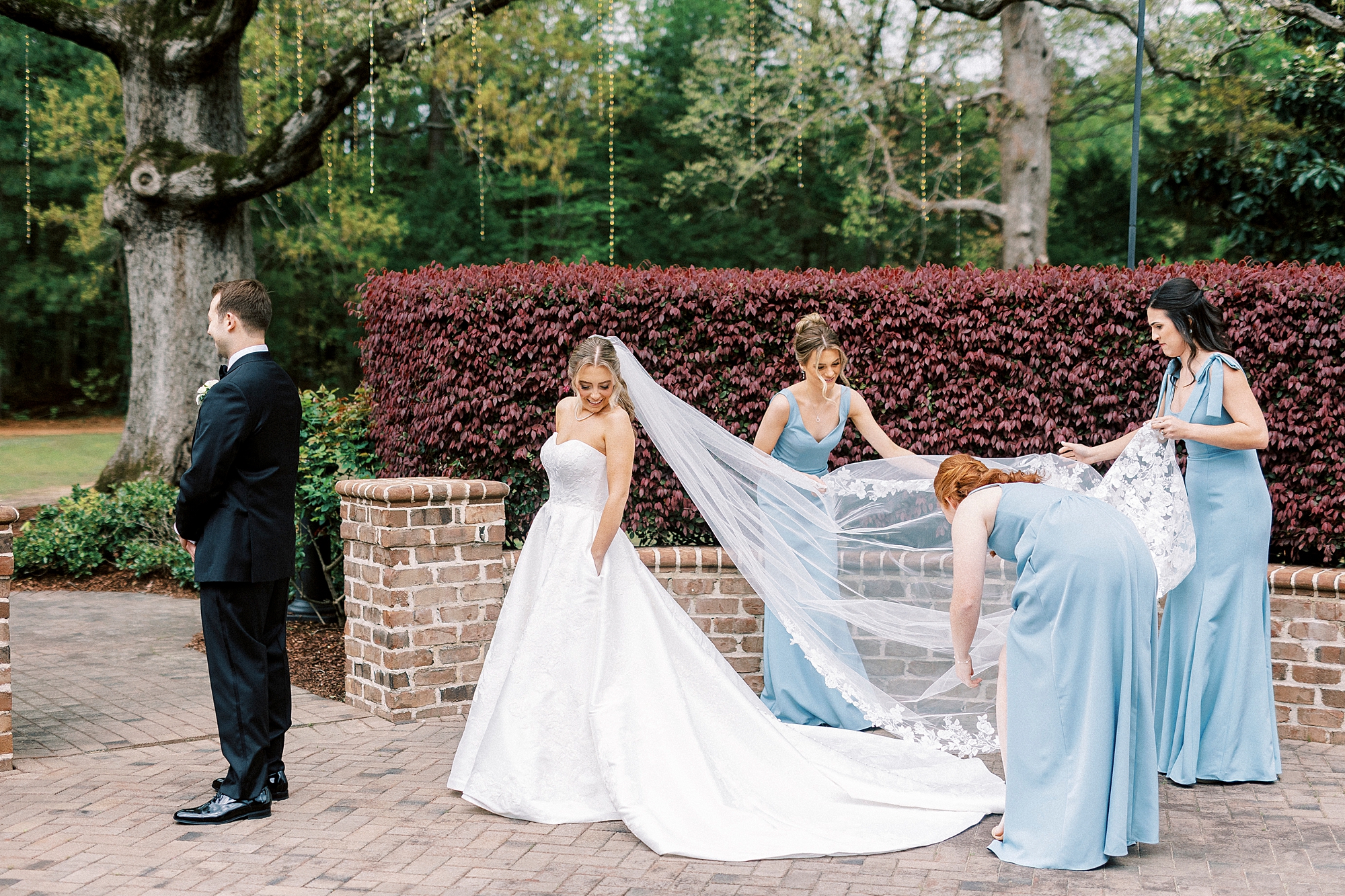 bridesmaids in light blue dresses help bride pull out veil