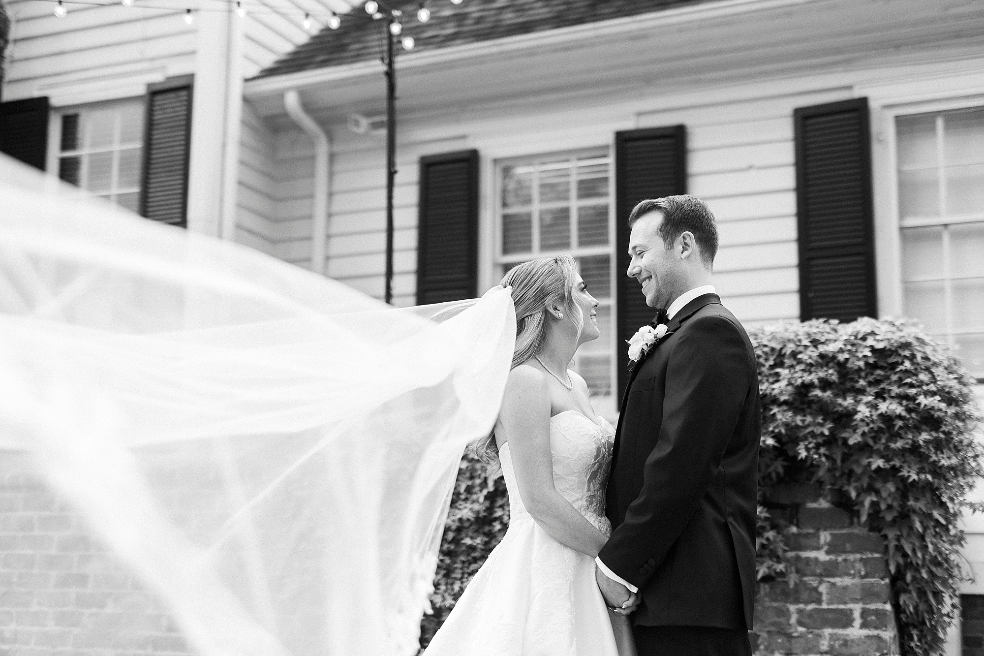 bride and groom smile at each other with bride's veil floating behind them 