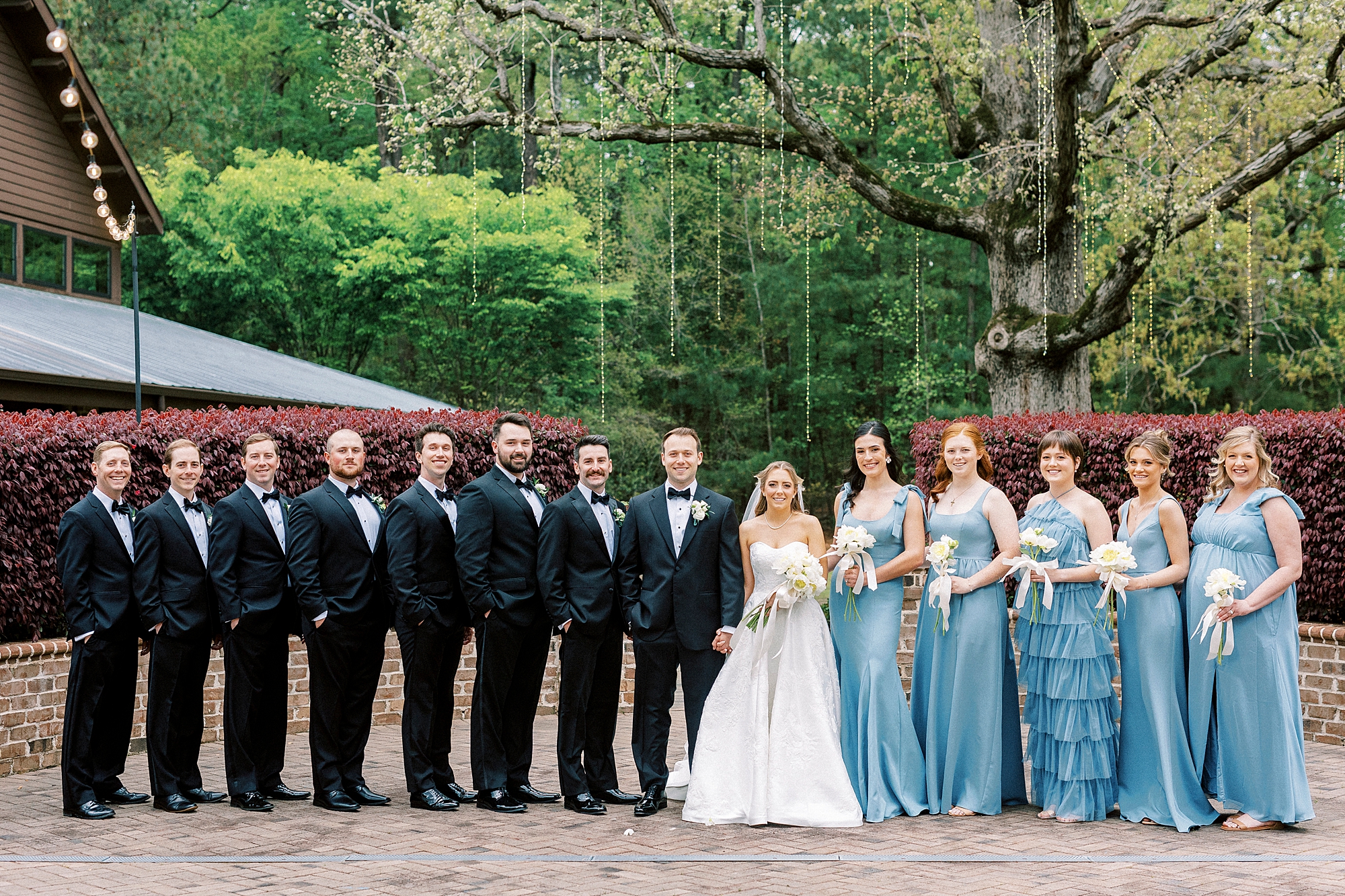 bride and groom stand in line with bridesmaids in light blue gowns and groomsmen in black suits 
