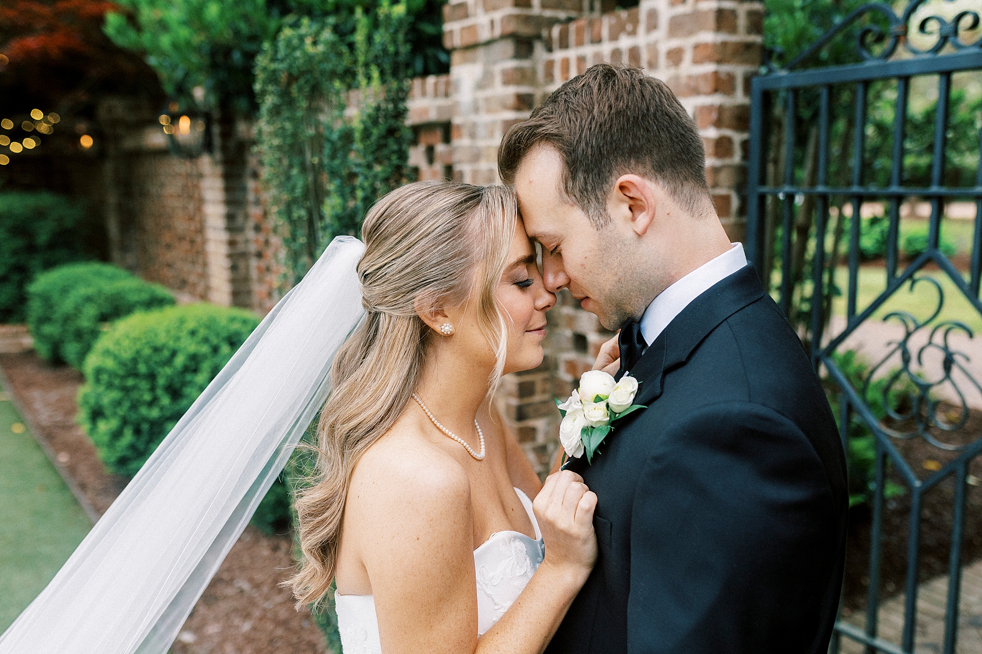 newlyweds lean heads together by brick archway at the Sutherland