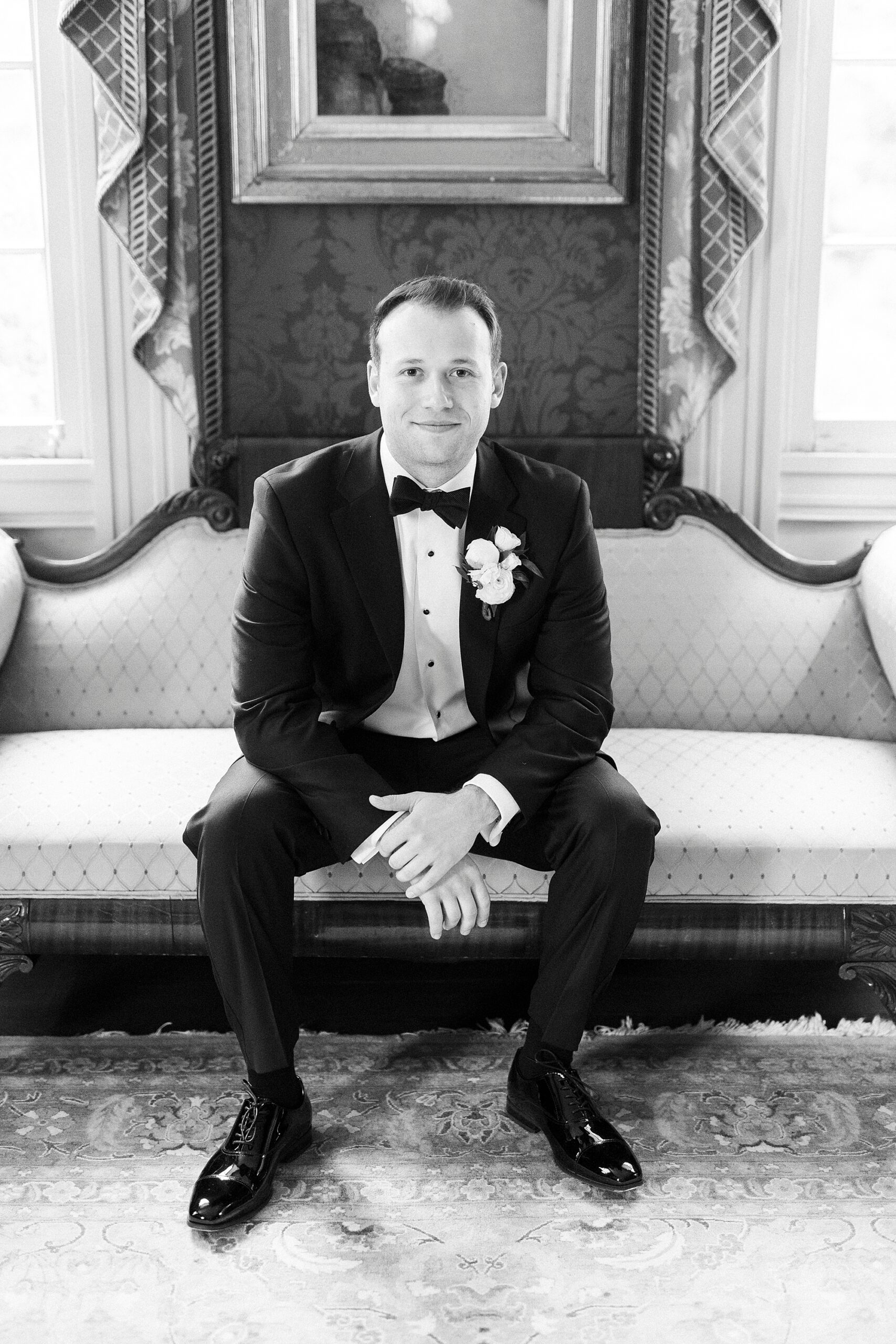 groom sits on vintage couch inside suite at the Sutherland