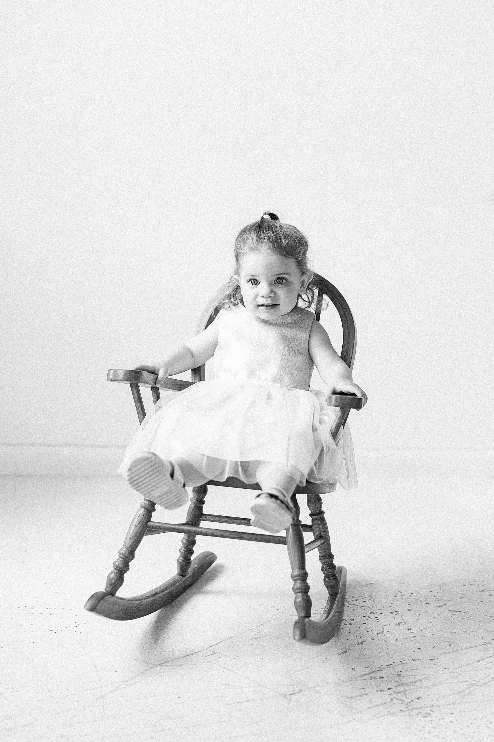 toddler sits in wooden rocking chair during Birthday Photos at Charlotte NC Photography Studio