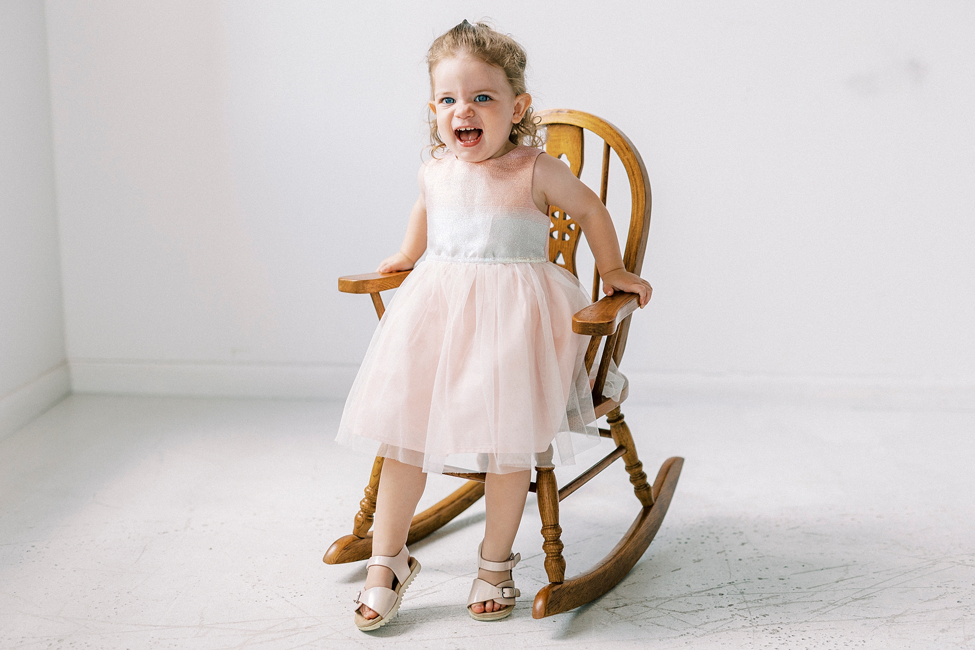 toddler in pink dress sits in wooden chair during Birthday Photos at Charlotte NC Photography Studio
