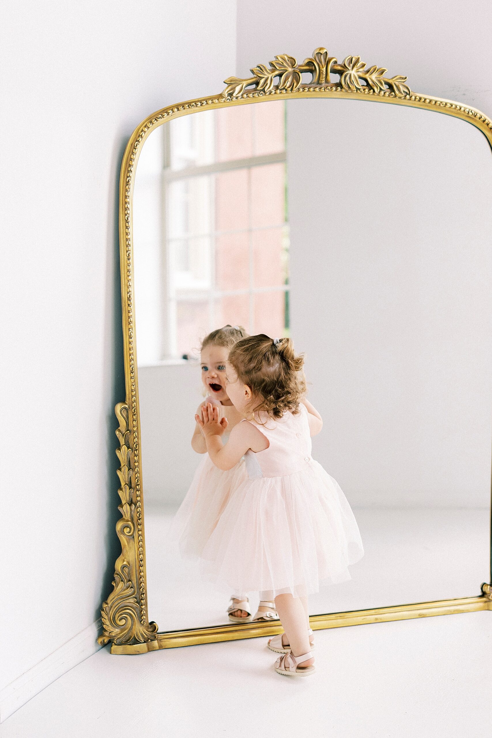 two year old leans against frame of mirror