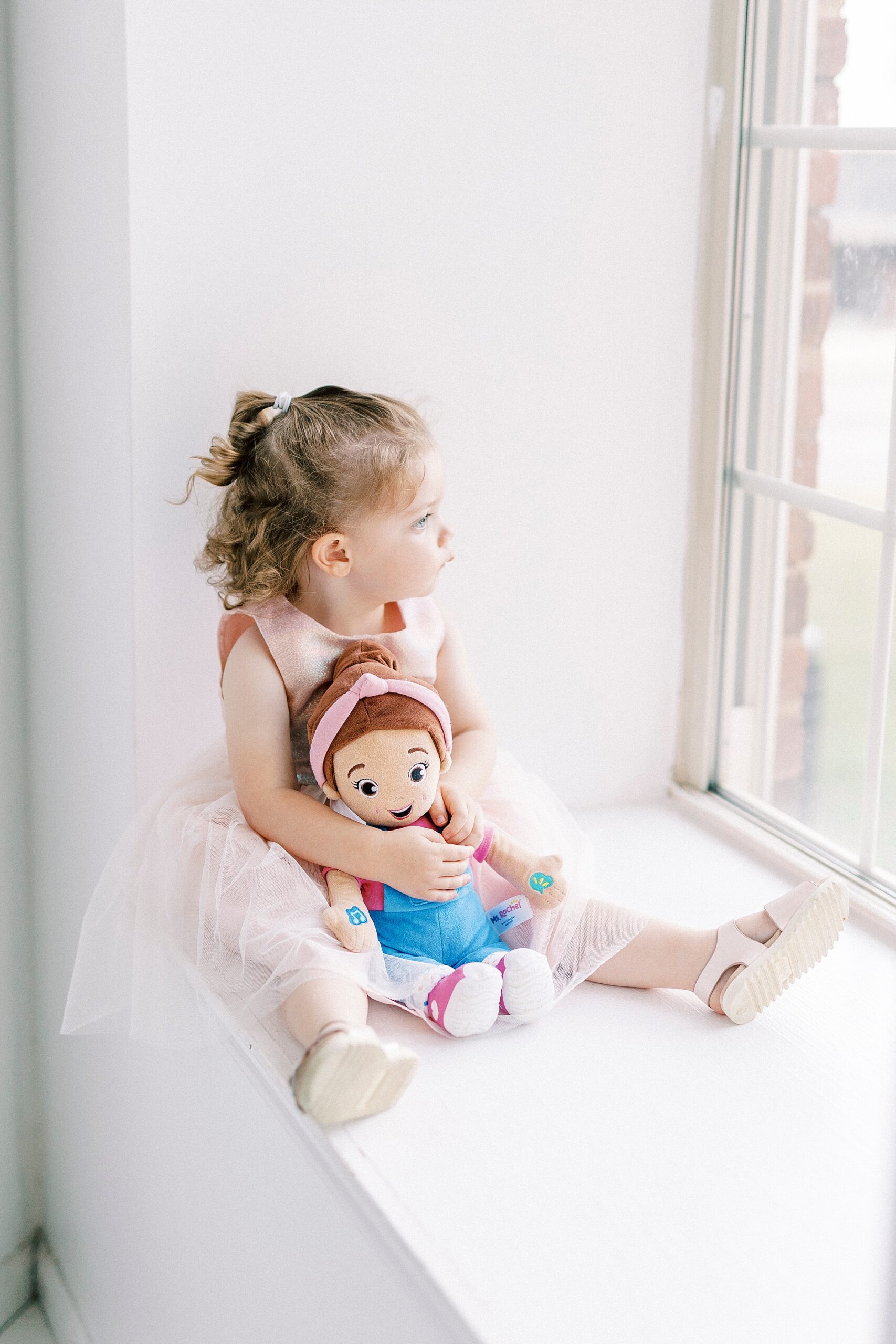 toddler hugs ms Rachel doll in window of photography studio