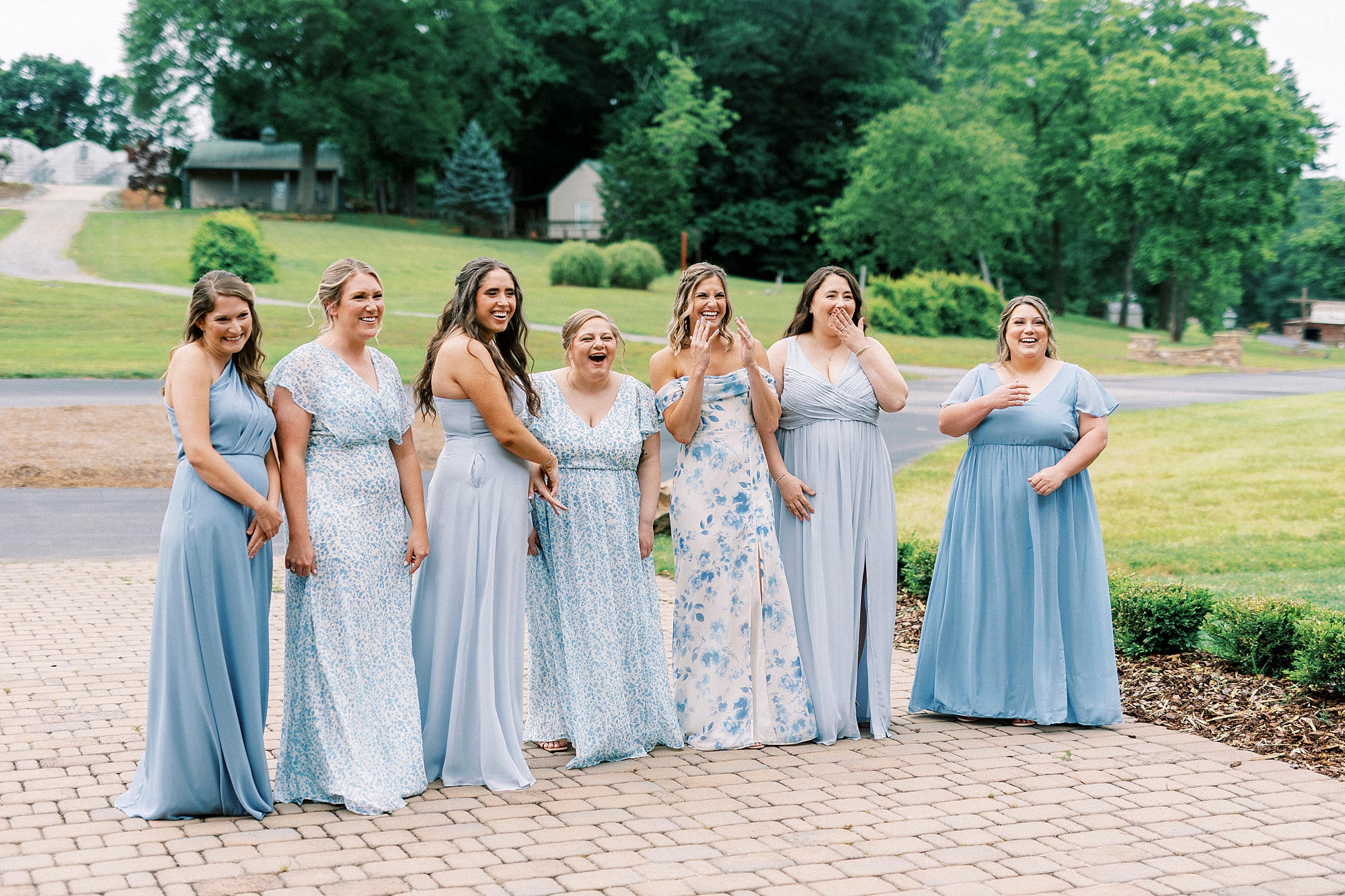 bridesmaids in mismatched light blue gowns gasp during first look with bride
