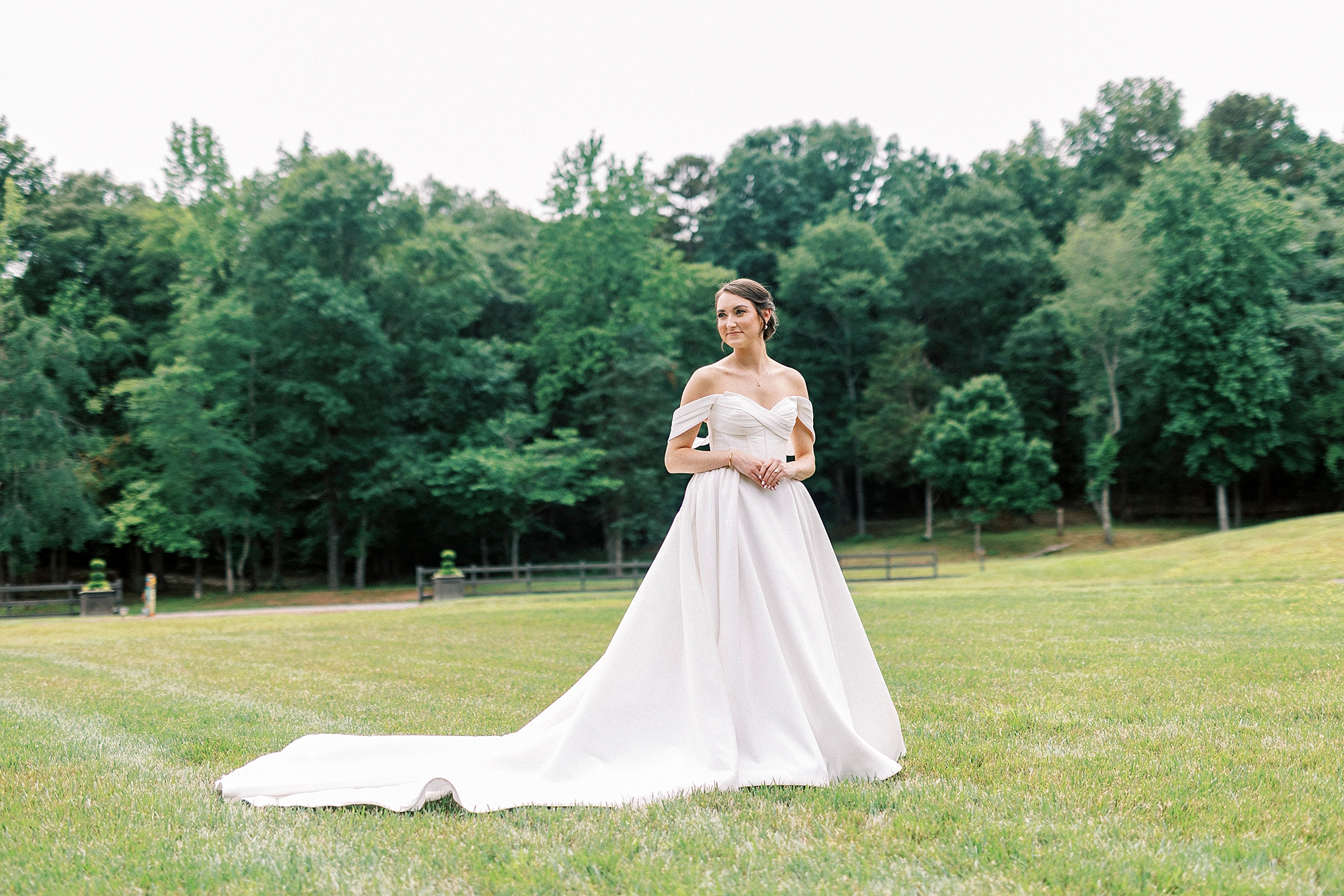 bride in off-the-shoulder gown turns standing on lawn