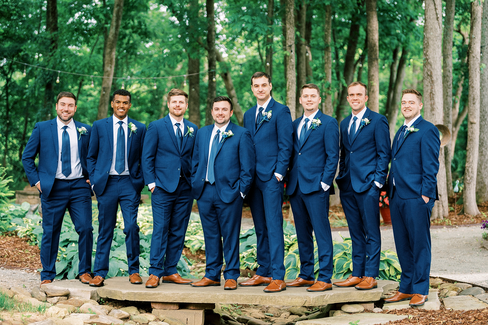 groom and groomsmen stand in line on stone wall 
