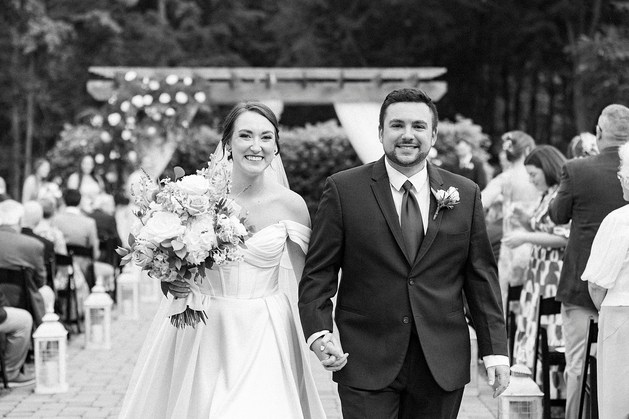 bride and groom hold hands walking up aisle away from pergola 