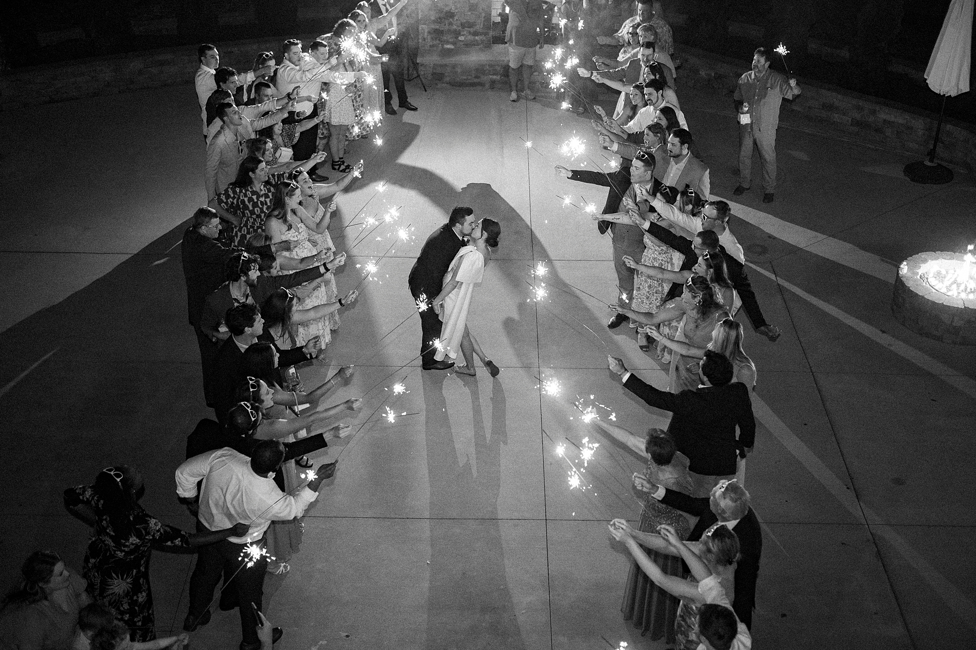 bride and groom kiss between guests holding sparklers 