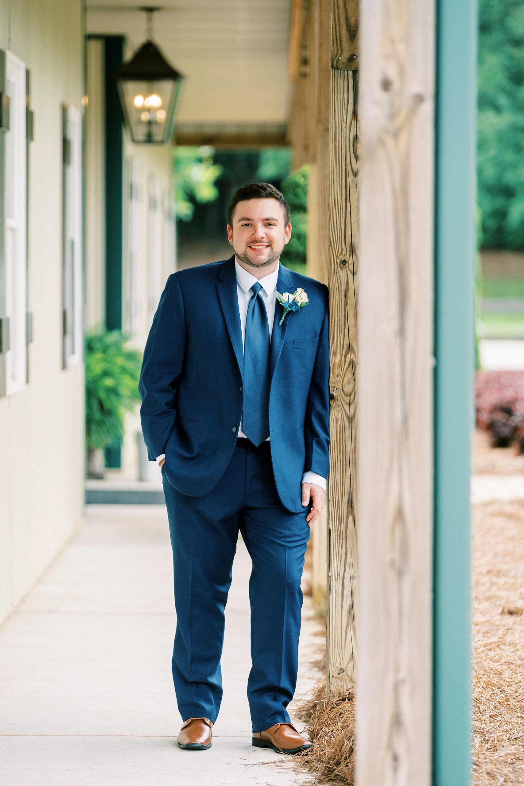 groom in navy suit leans against wooden pillar