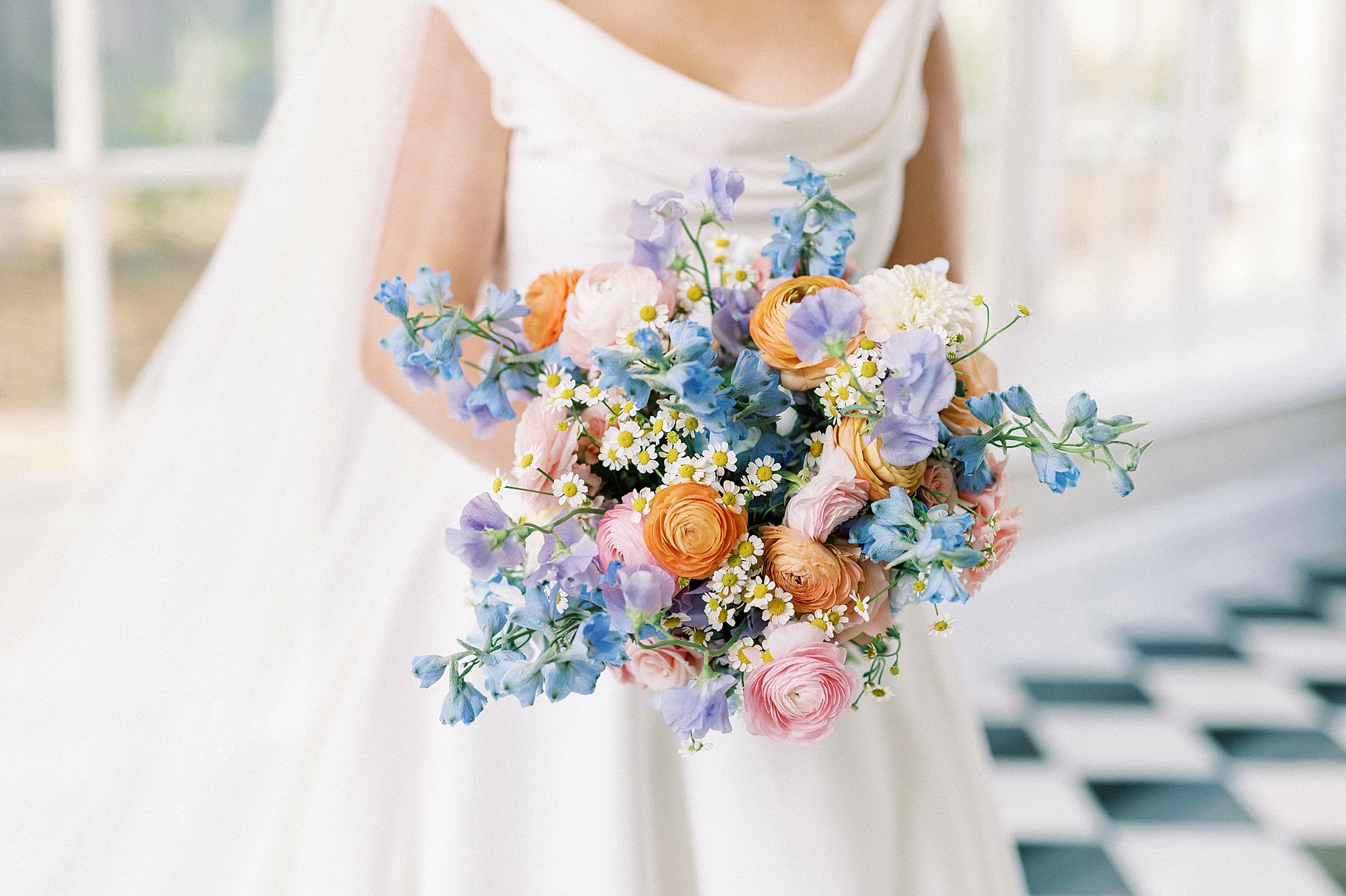 bride holds spring bouquet of pastel flowers in front of classic wedding gown