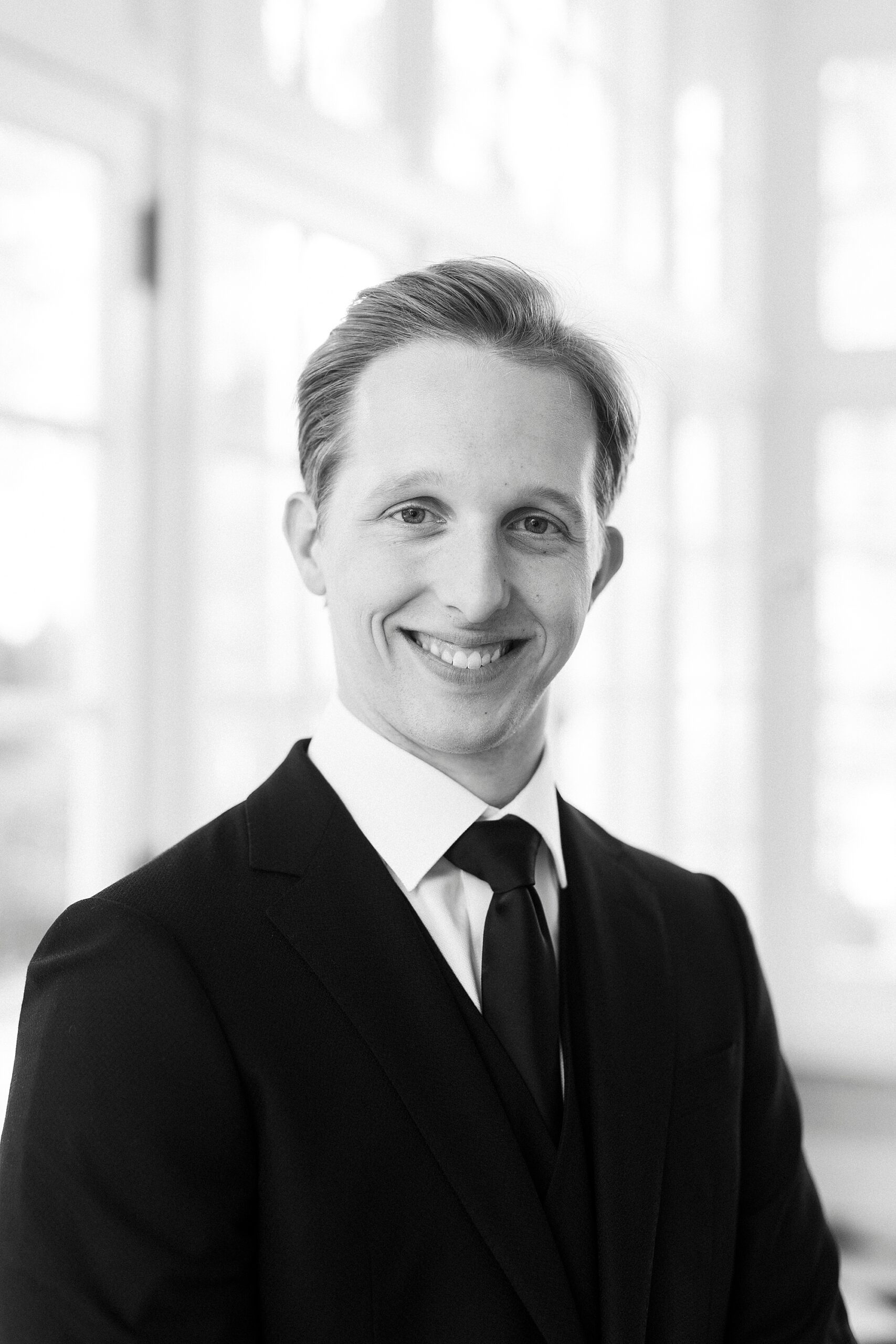 groom smiles in black suit with black tie