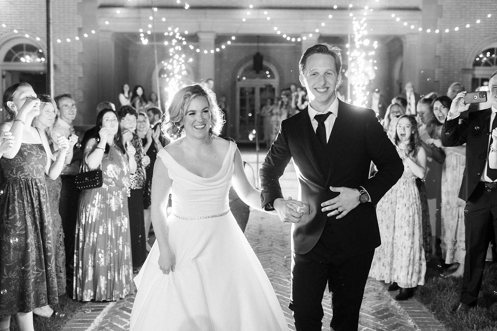 groom holds hands with bride leading her out of sparkler exit