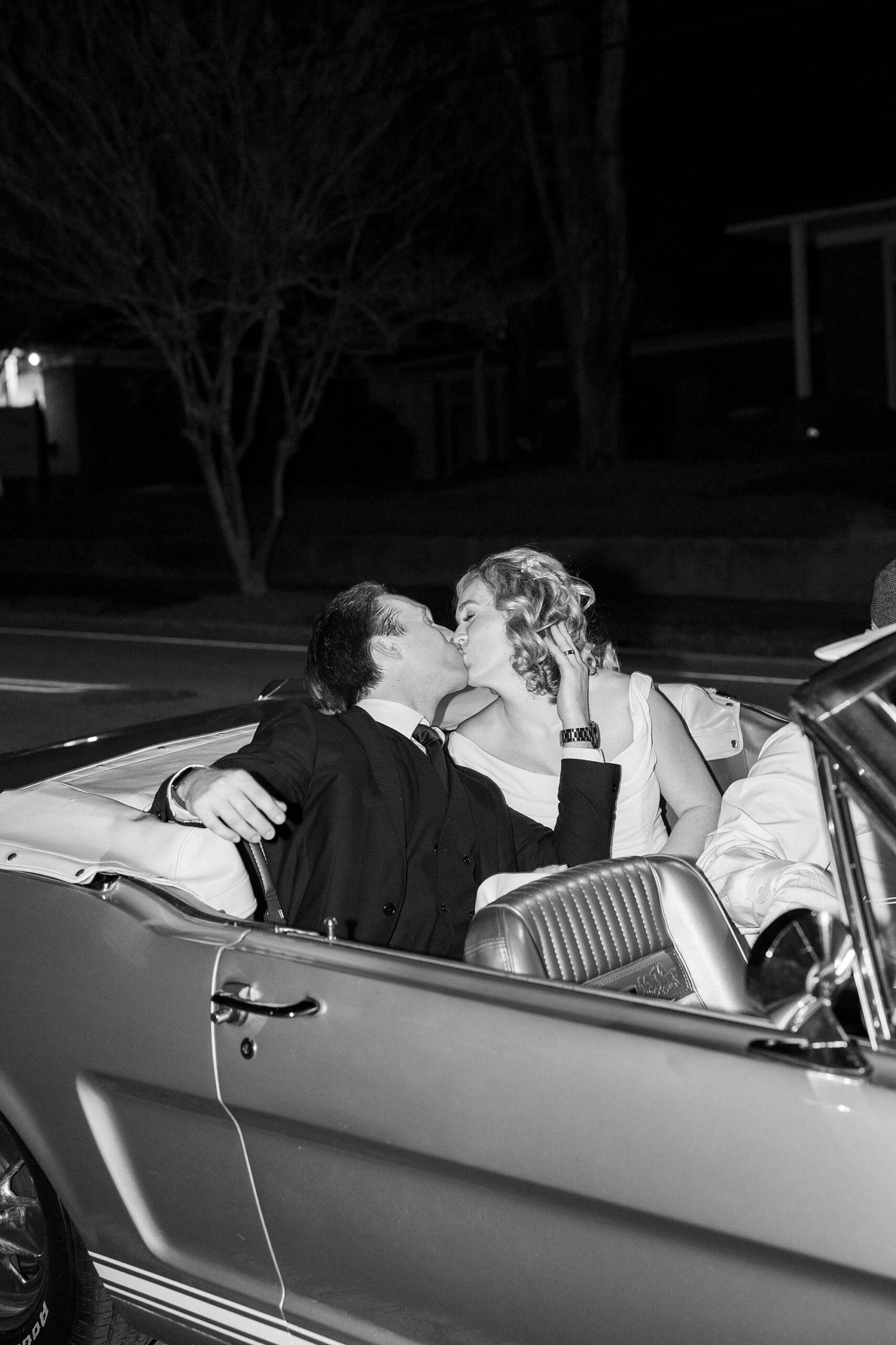 bride and groom kiss in back of convertible 