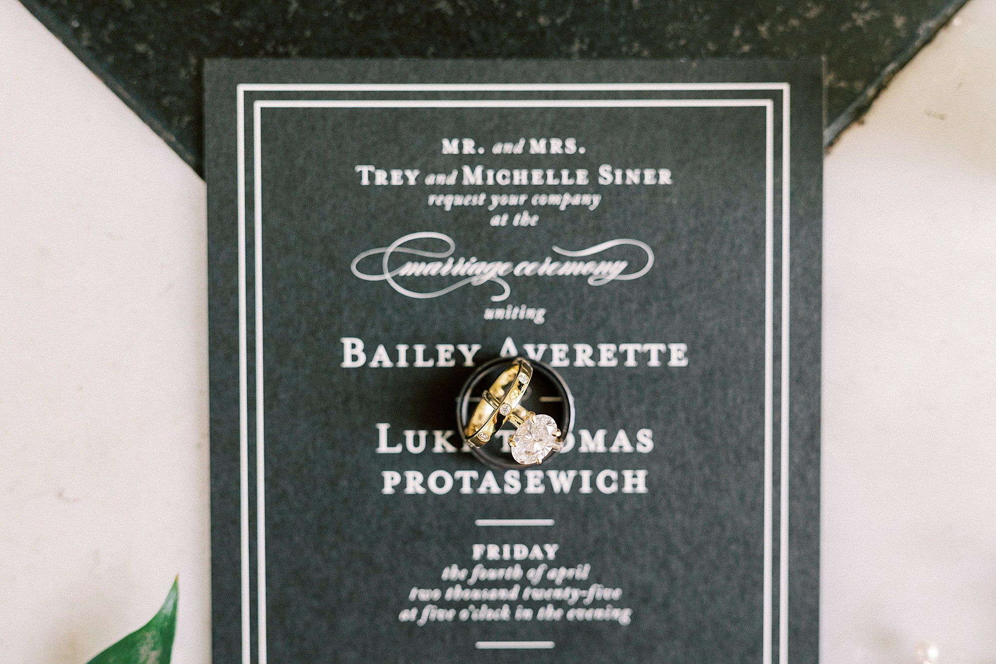 gold wedding bands rest on black and white invitation suite 