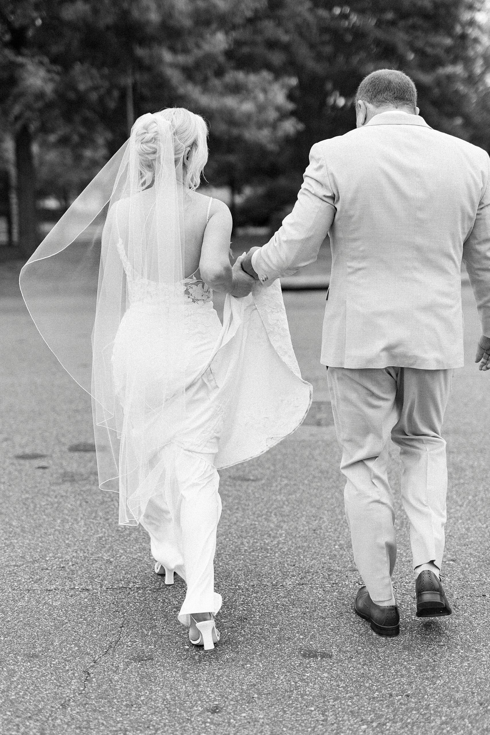 man helps bride walk by carrying back of her wedding dress