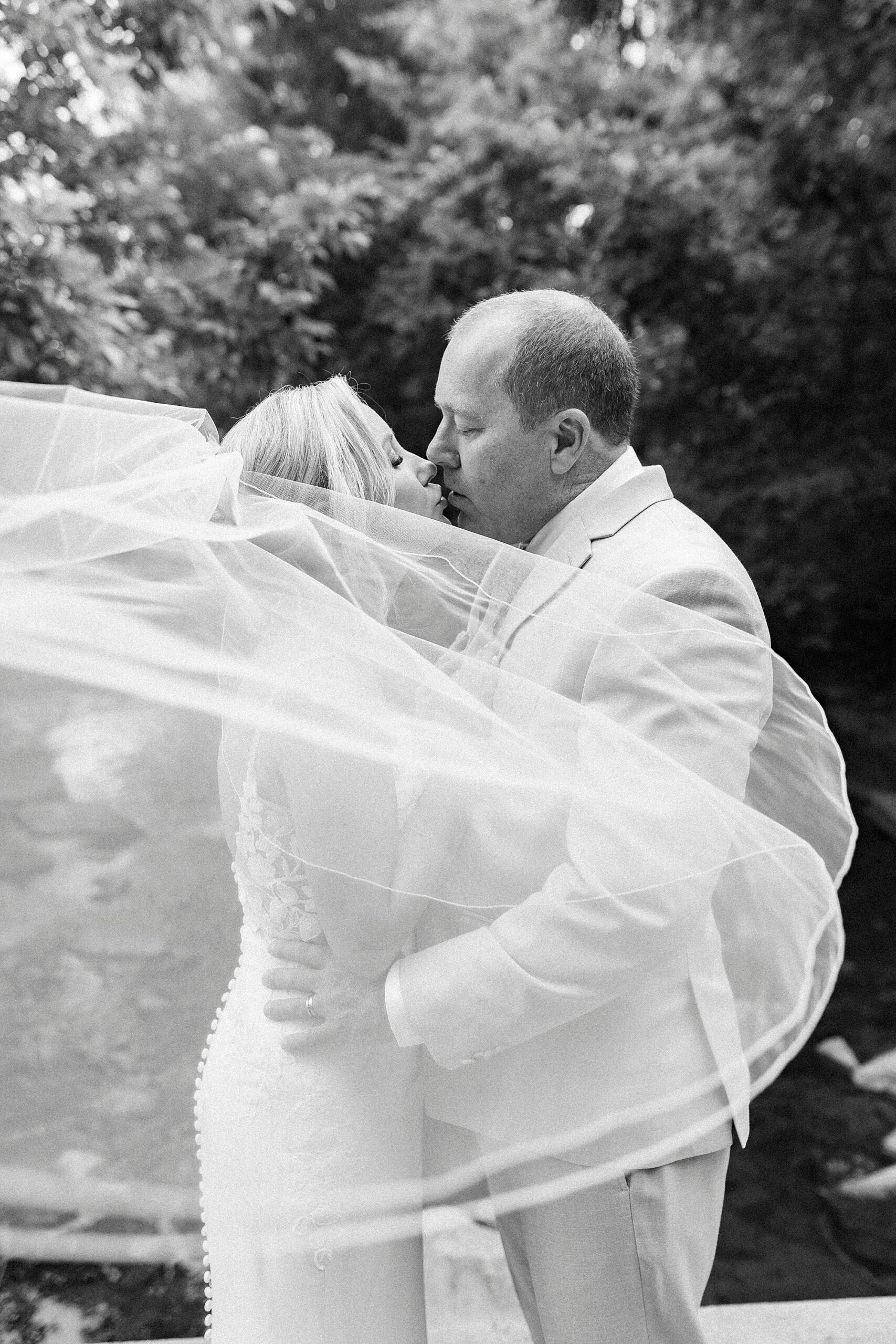 bride and groom kiss with veil blowing around them