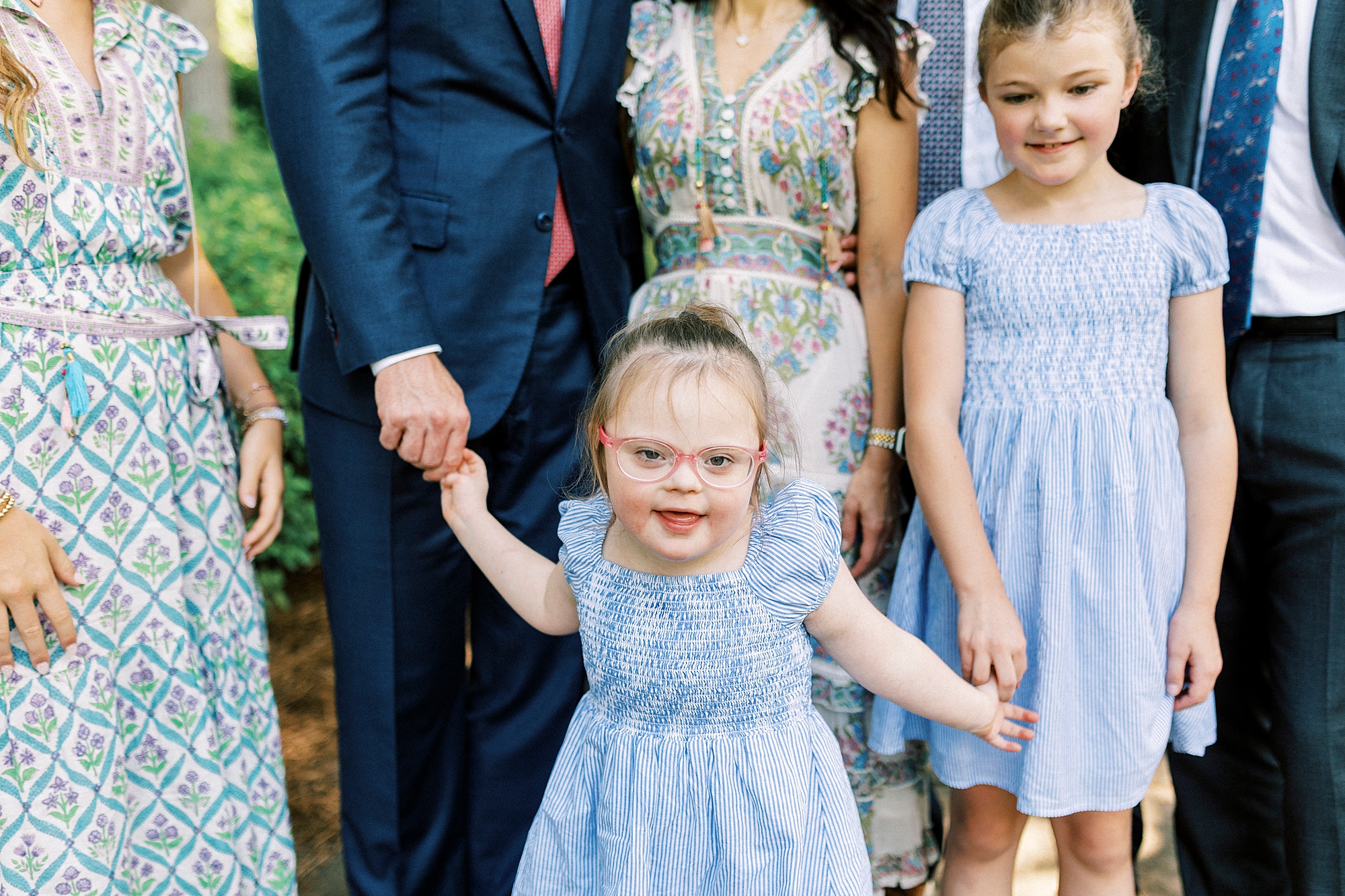 dad holds hands with daughter with Down syndrome while she smiles at camera