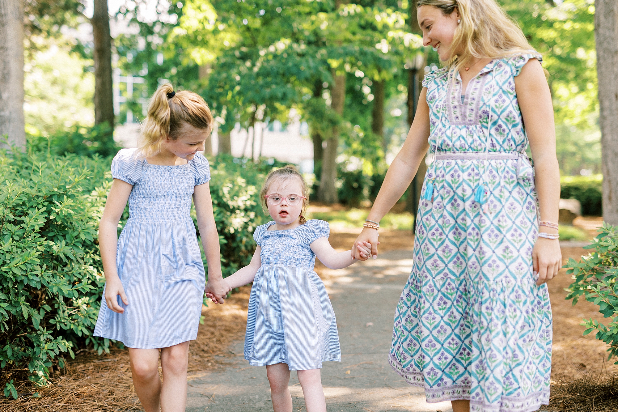 three sisters hold hands walking in blue dresses in Cullman Park