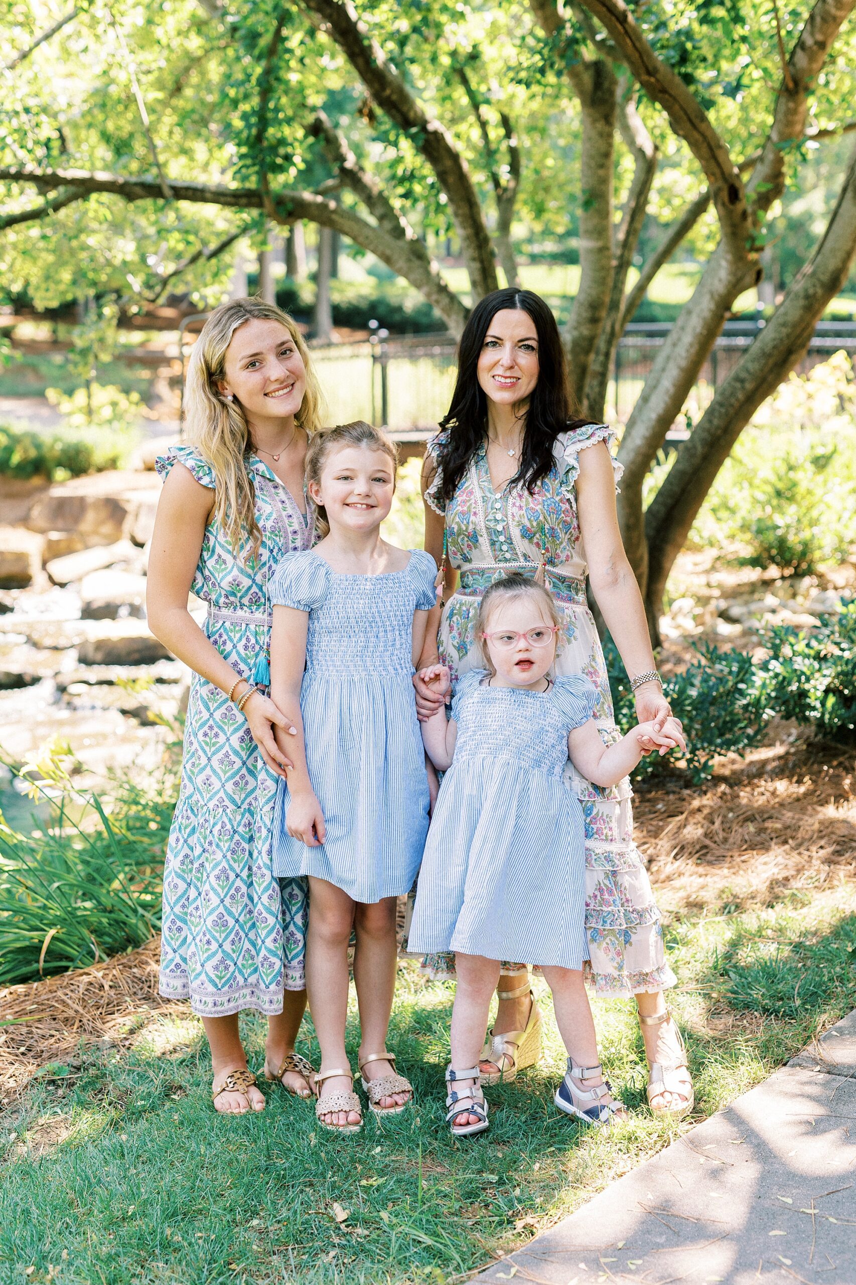 mom poses with three daughters under tree in park