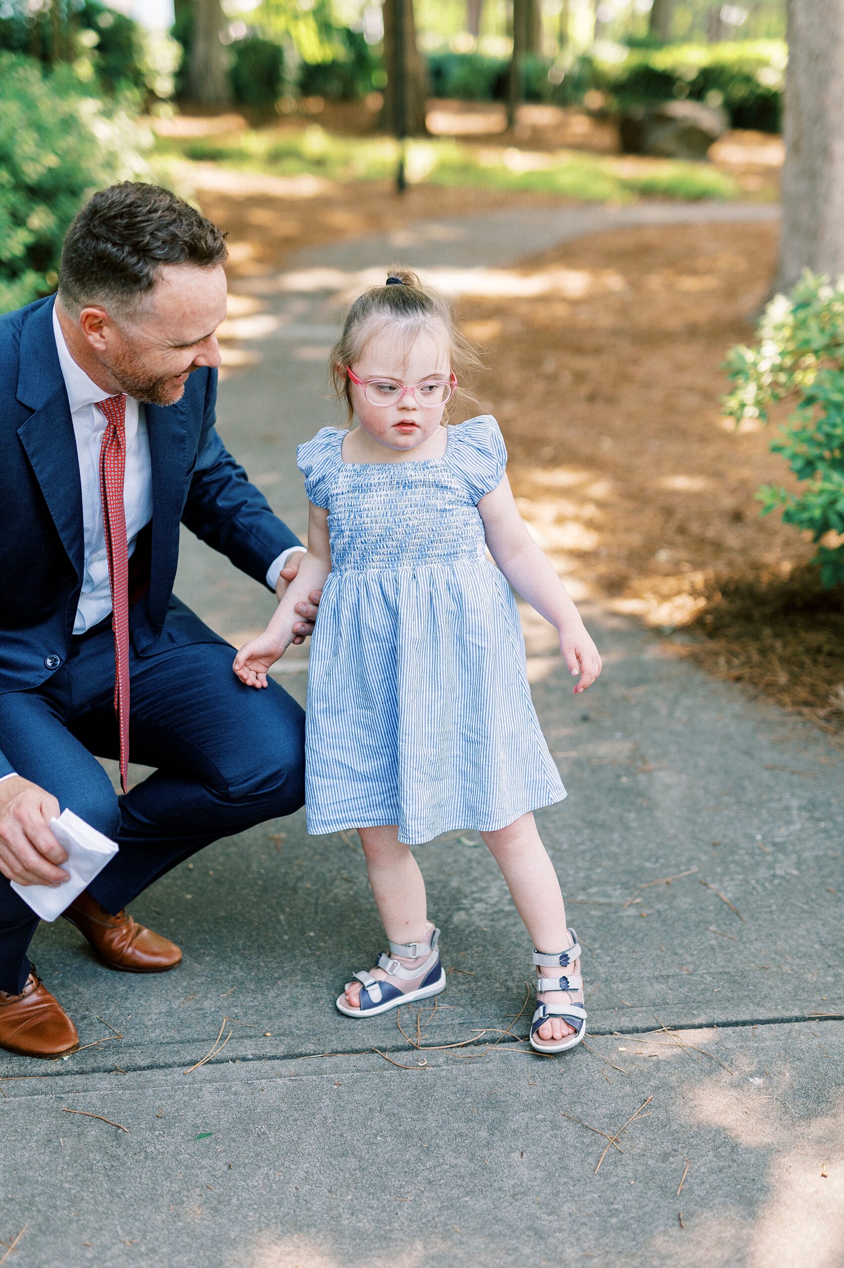 dad kneels down to talk with daughter with Down syndrome in park