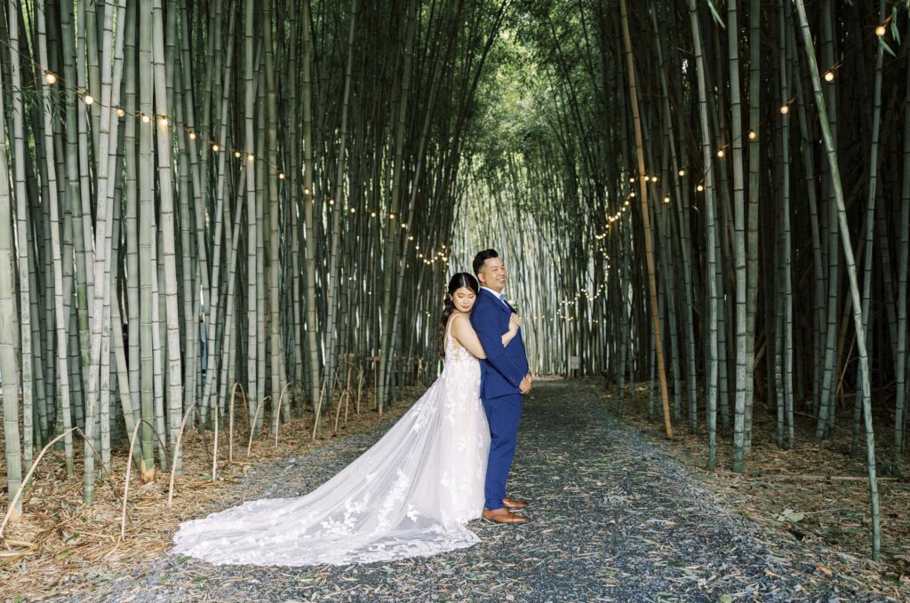 bride hugs groom from behind in front of large bamboo forest at Camelot meadows wedding venue