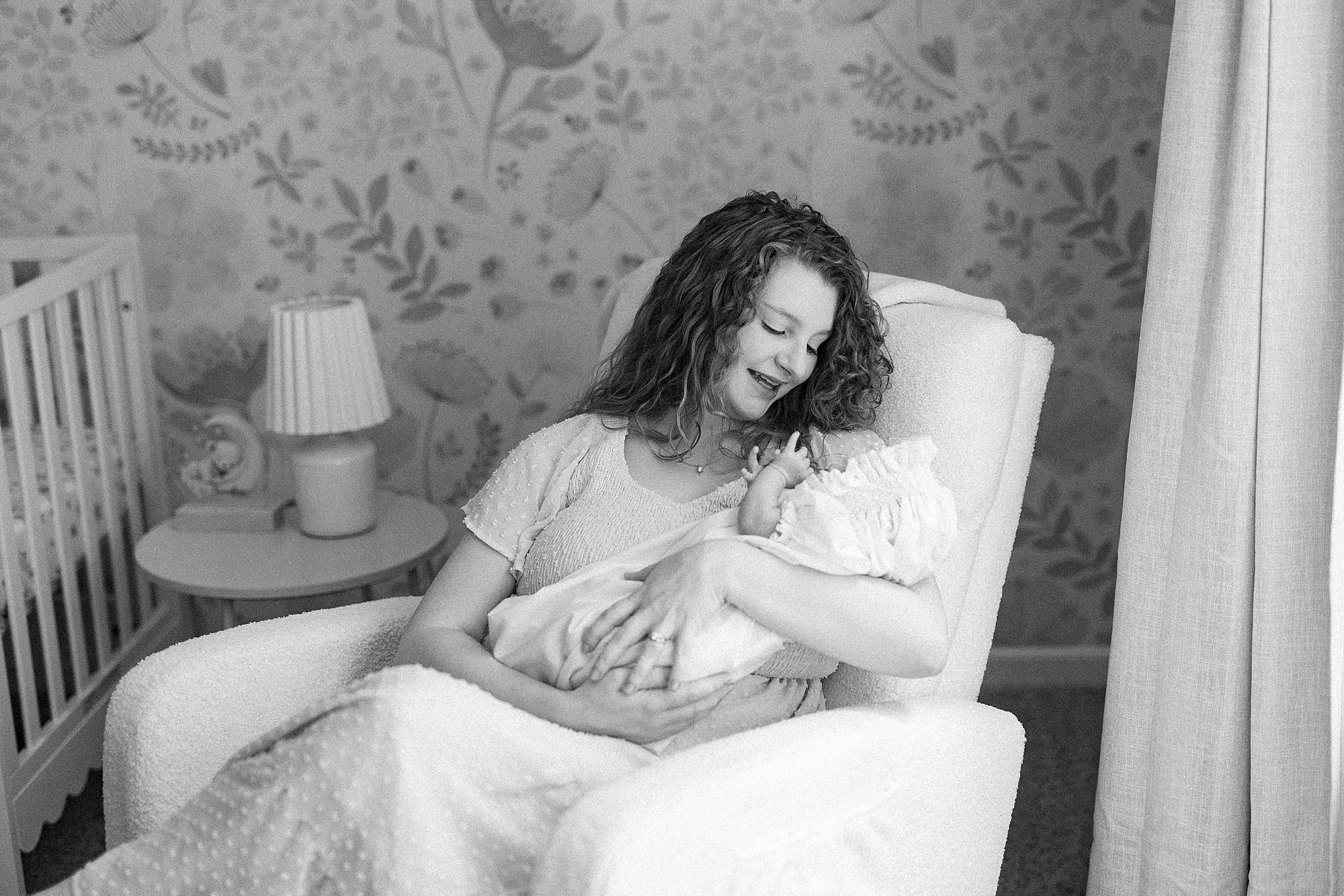 mom rocks baby girl in corner of nursery during lifestyle newborn session with Winston-Salem family photographer