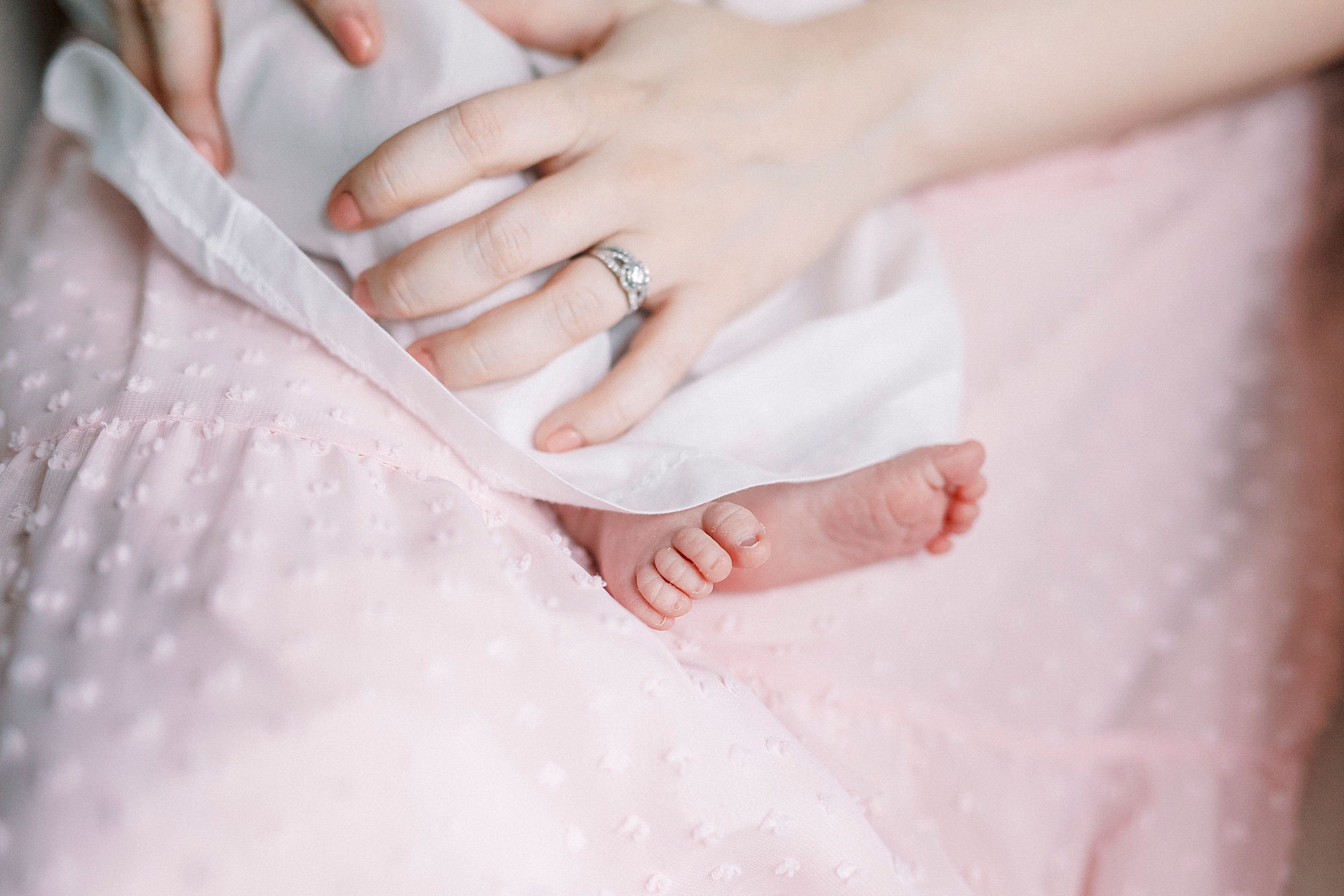 mom holds baby's legs in white dress during lifestyle newborn session with Winston-Salem family photographer
