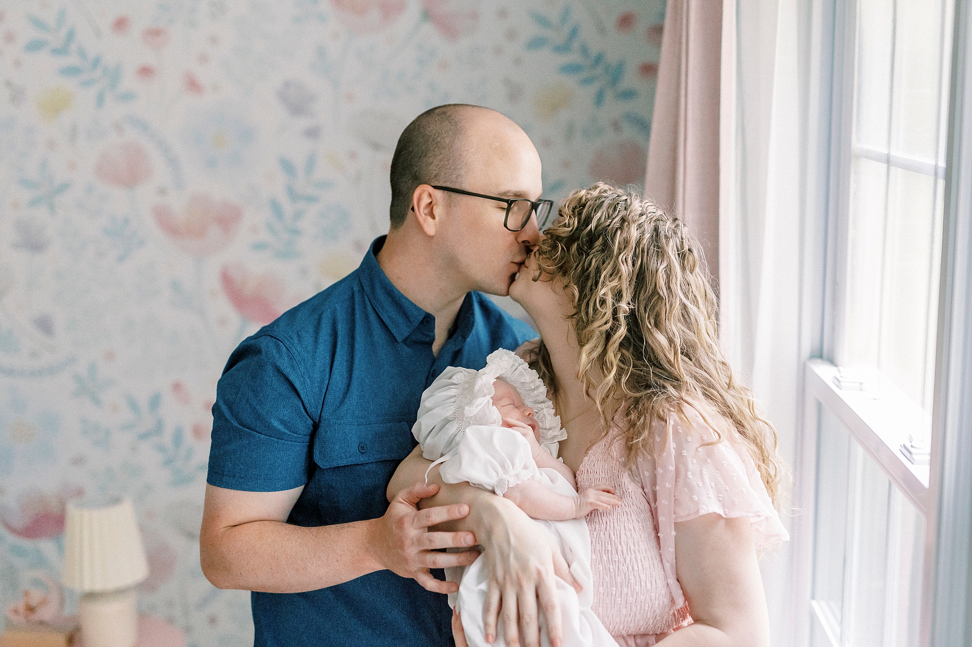 parents kiss by window in nursery during lifestyle newborn session with Winston-Salem family photographer