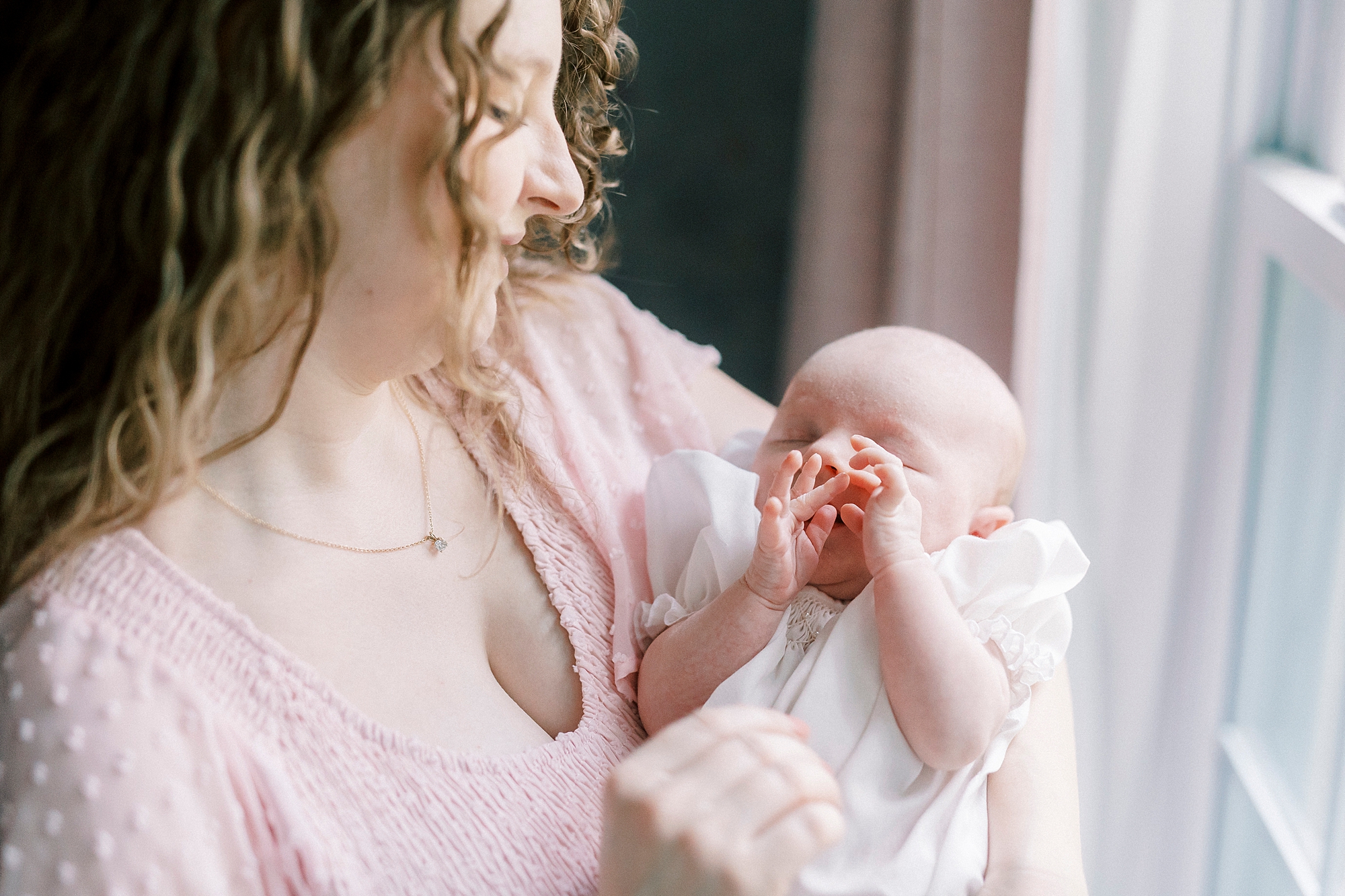 mother in pink dress holds newborn baby girl during lifestyle newborn session with Winston-Salem family photographer