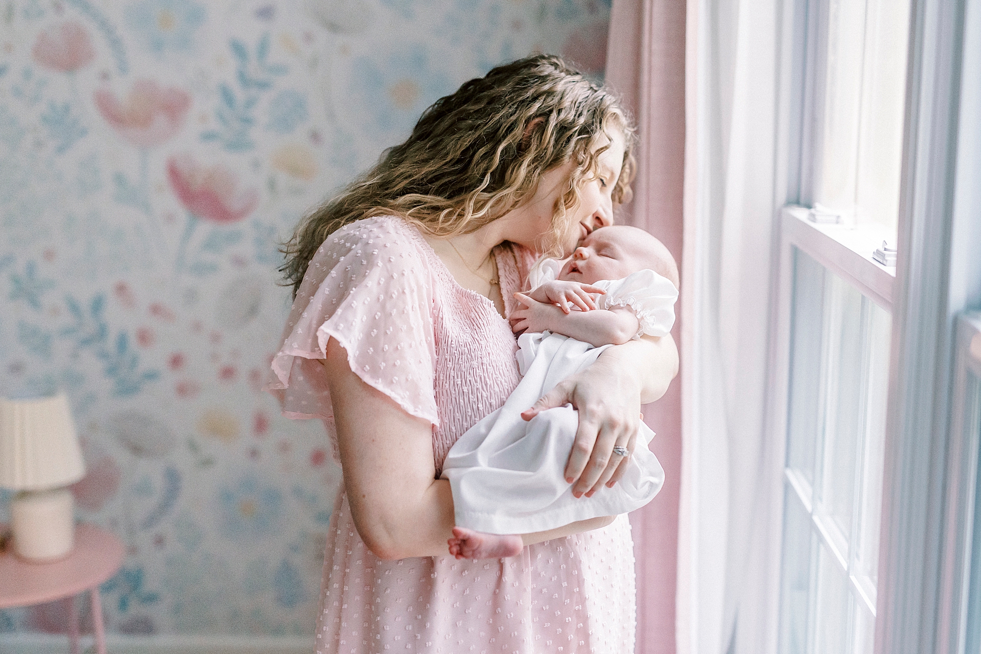 mom in pink dress leans to kiss baby's forehead 