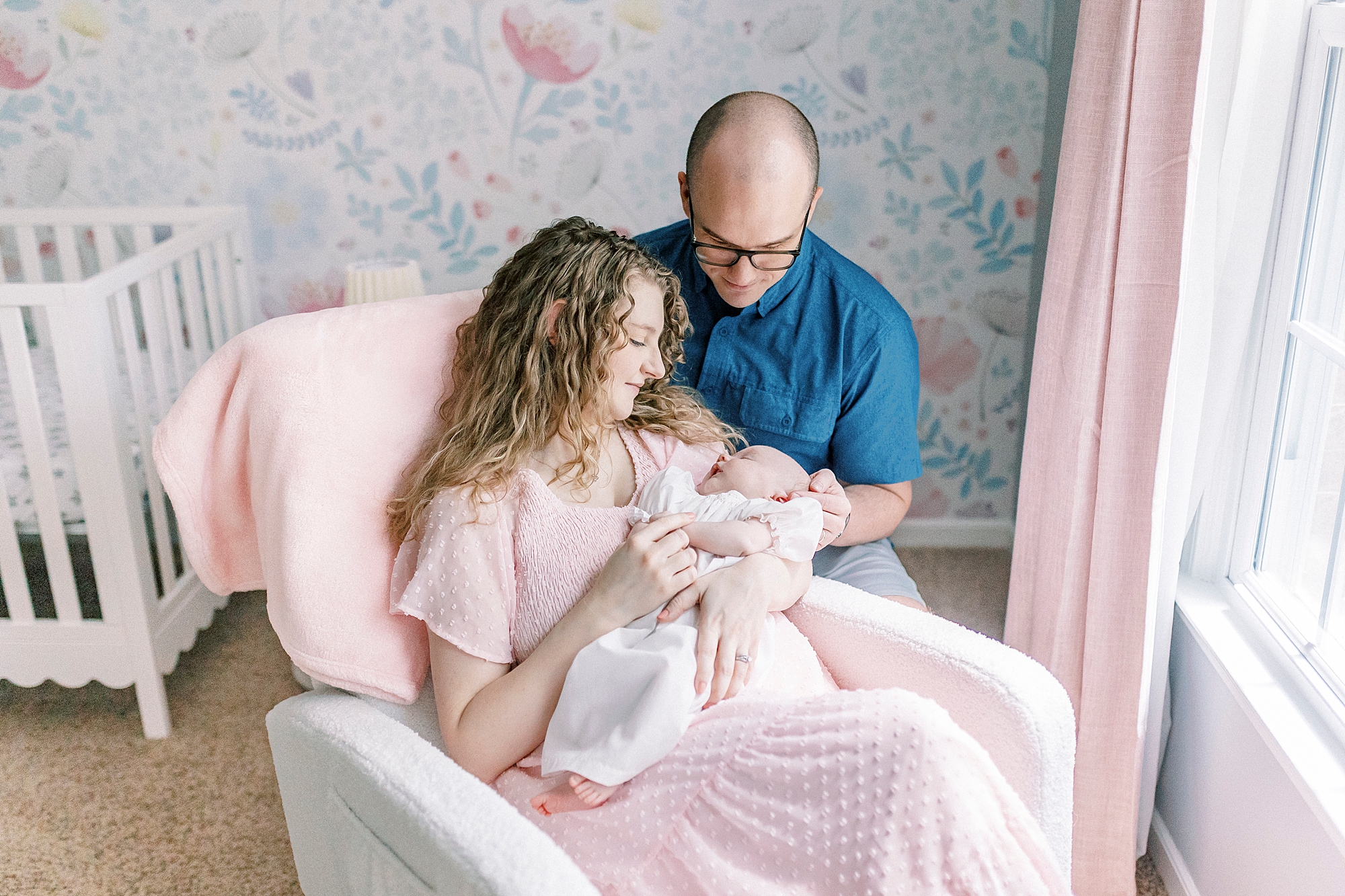 new parents snuggle baby in rocker in nursery during lifestyle newborn session with Winston-Salem family photographer